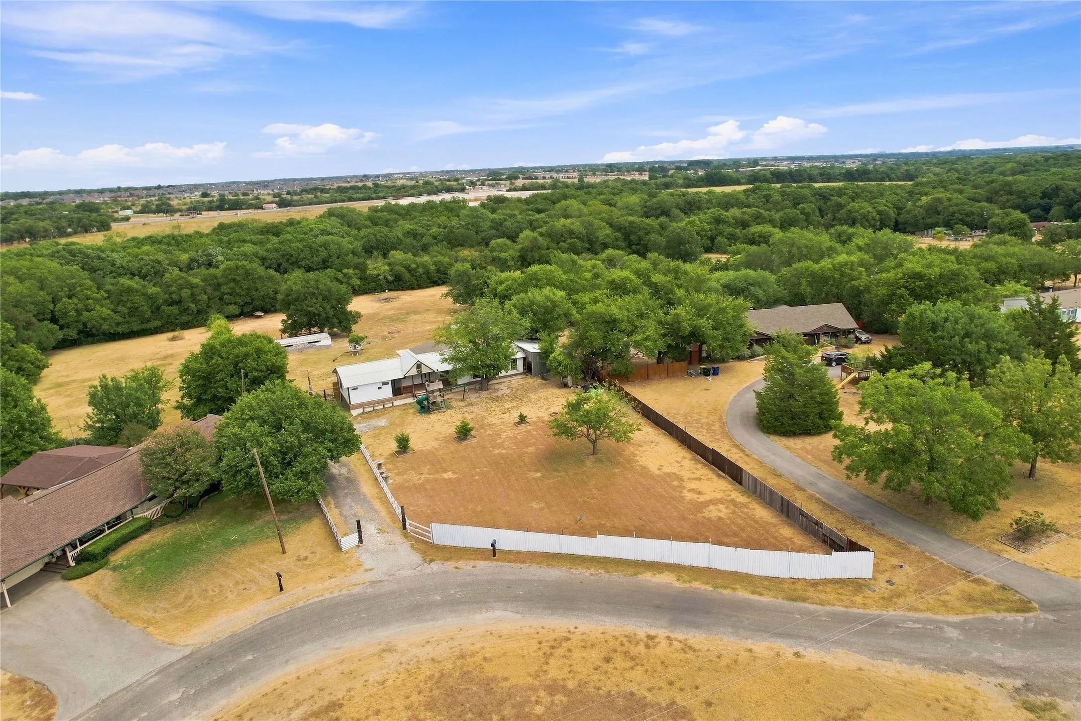 Expansive property featuring multiple mature trees, a private driveway, and a fenced perimeter