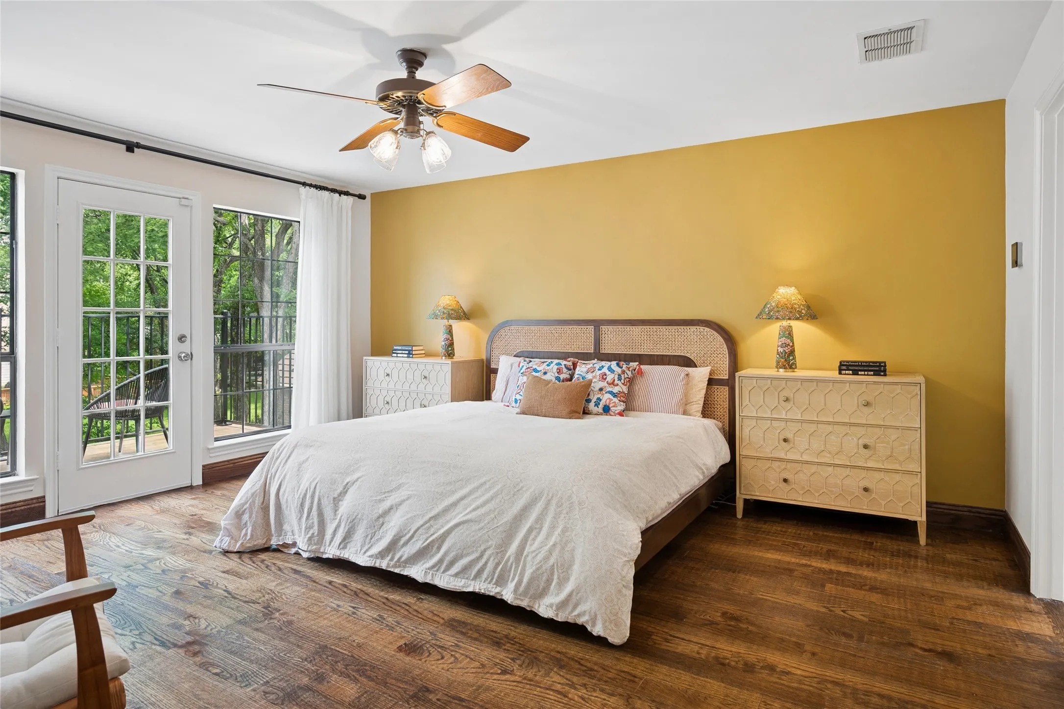 The spacious primary bedroom with hardwood floors upstairs, features a private balcony retreat overlooking the lush backyard, pool, and creek.