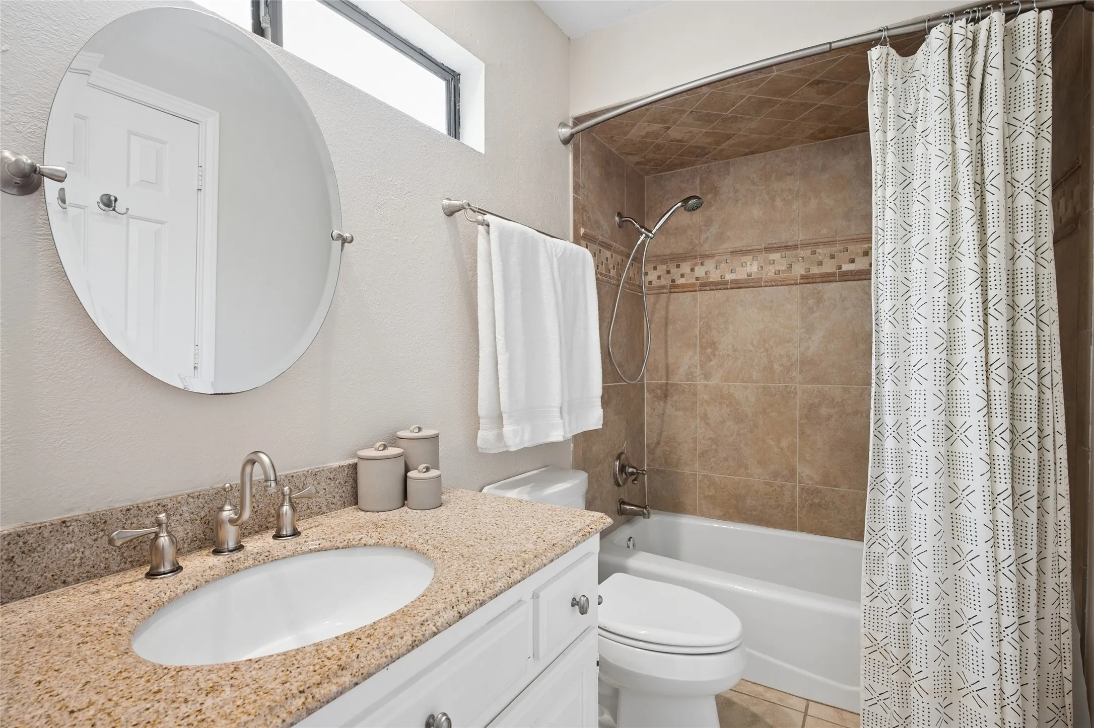 Ensuite bathroom features earthy toned granite counters, a decorative mirror, and tile tub surround.