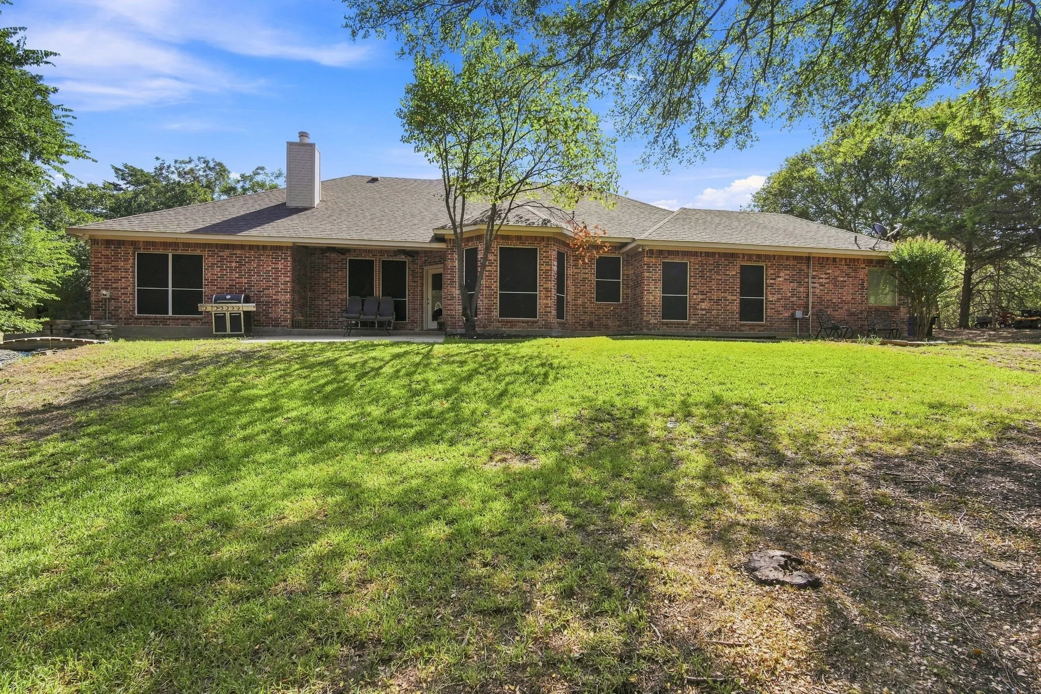 Unwind on the covered patio surrounded by mature trees and a picturesque stone chimney, a true backyard oasis made for morning coffee or evening gatherings.