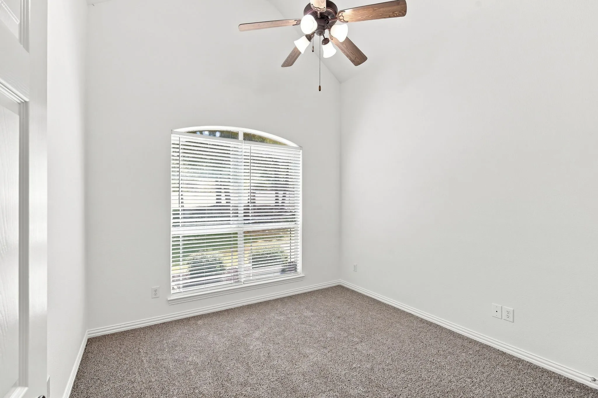 Bright bedroom with a vaulted ceiling, lighted ceiling fan, and an arched window that fills the room with natural light.