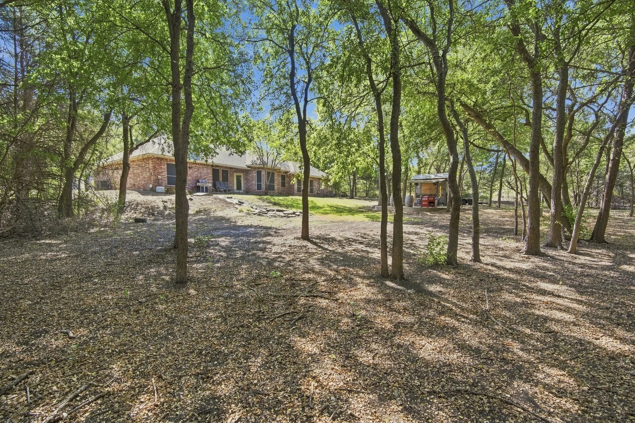 Step into your own backyard paradise, featuring a covered patio with stone hardscaping, towering shade trees, and a charming detached structure perfect for relaxing or entertaining.