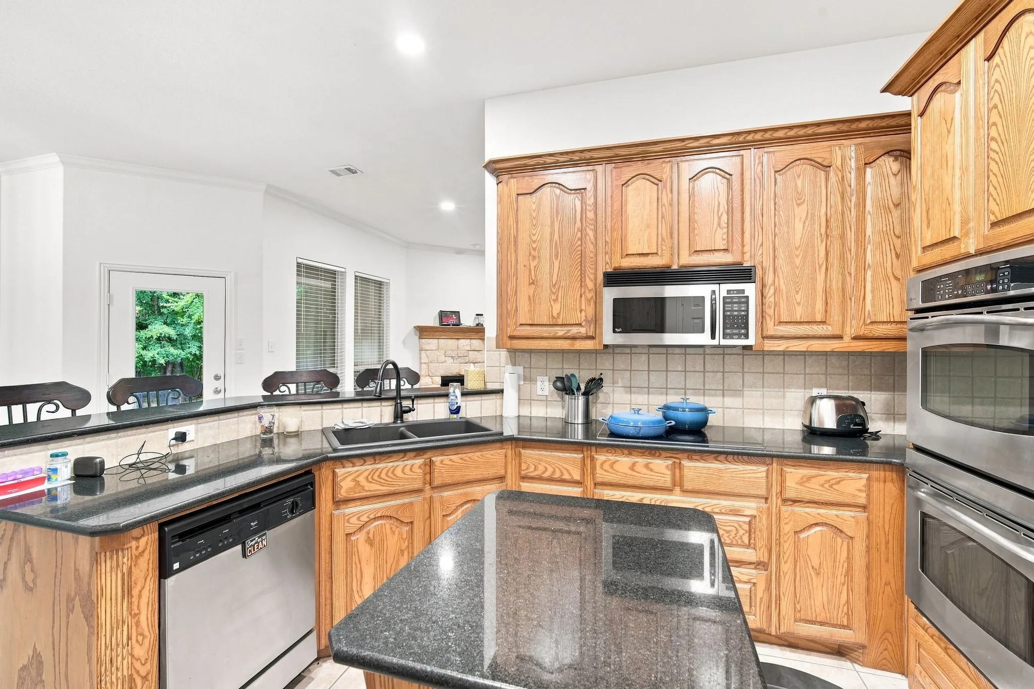 Stylish kitchen with wood cabinetry, sleek granite countertops, a dual-basin sink and tile backsplash.