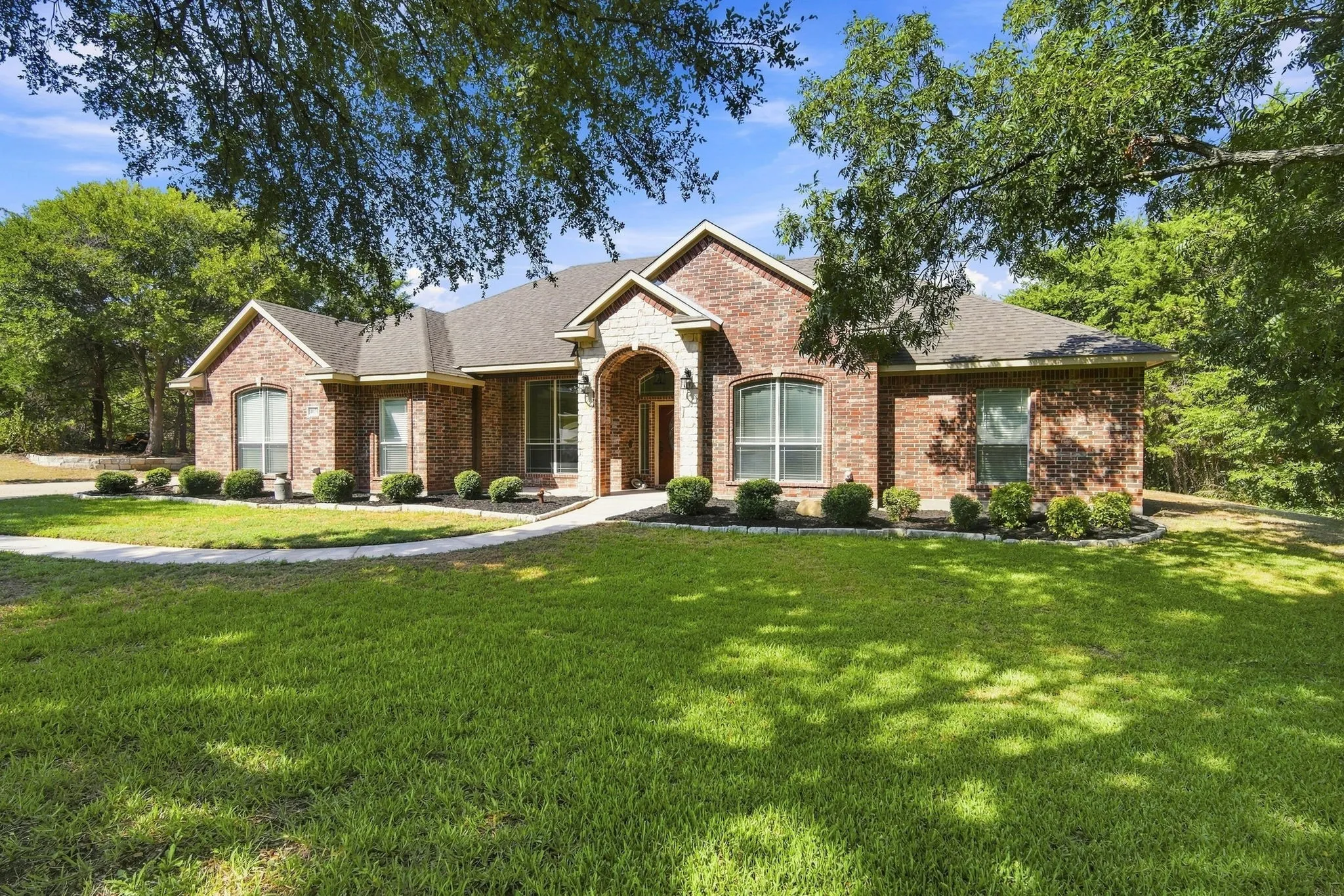 Handsome brick and stone facade with an arched entry, tall windows, and a beautifully landscaped walkway welcoming you home.