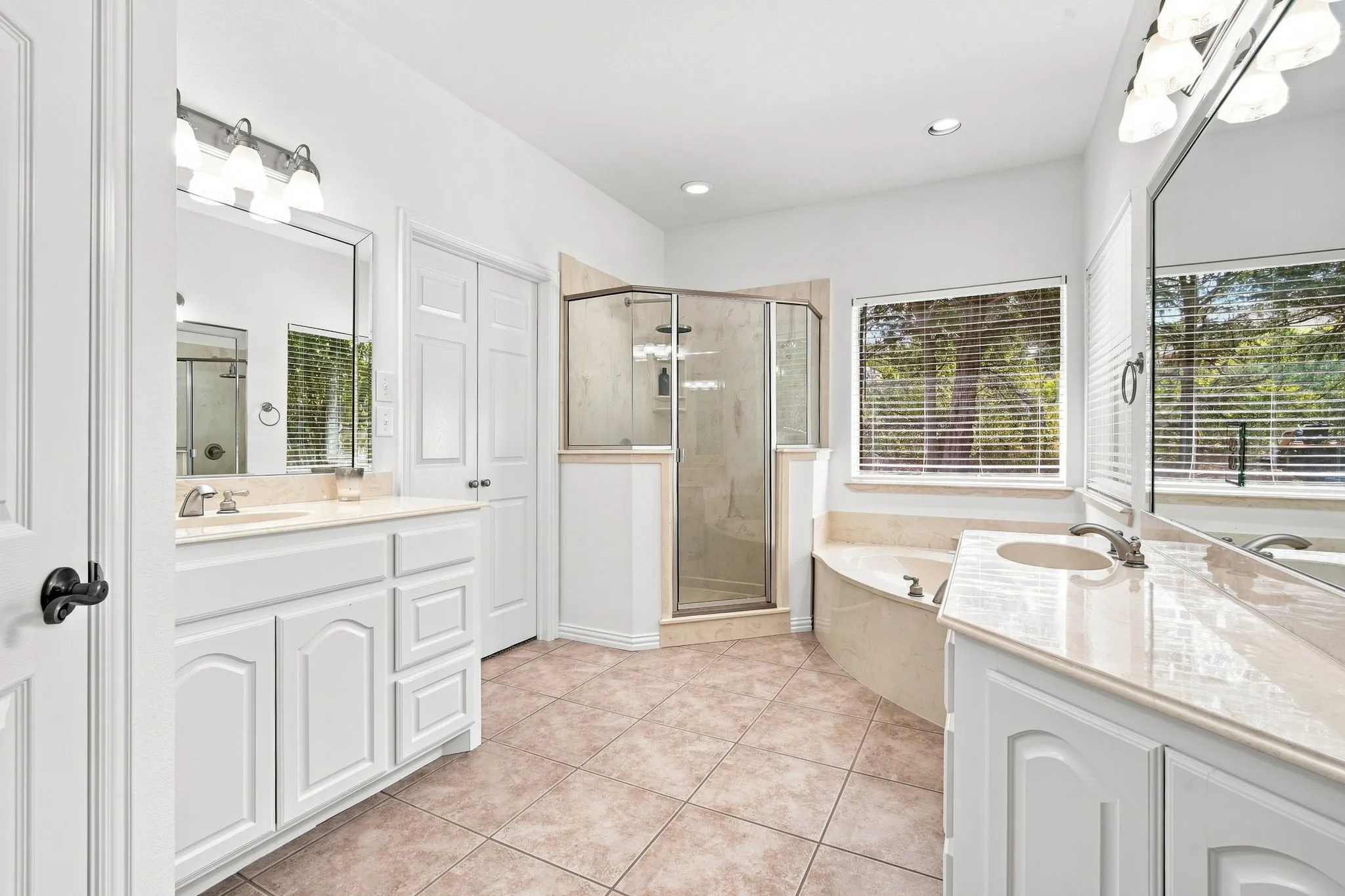 Spa-like primary bath with dual vanities, a glass-enclosed shower, a soaking tub, and elegant tile flooring.