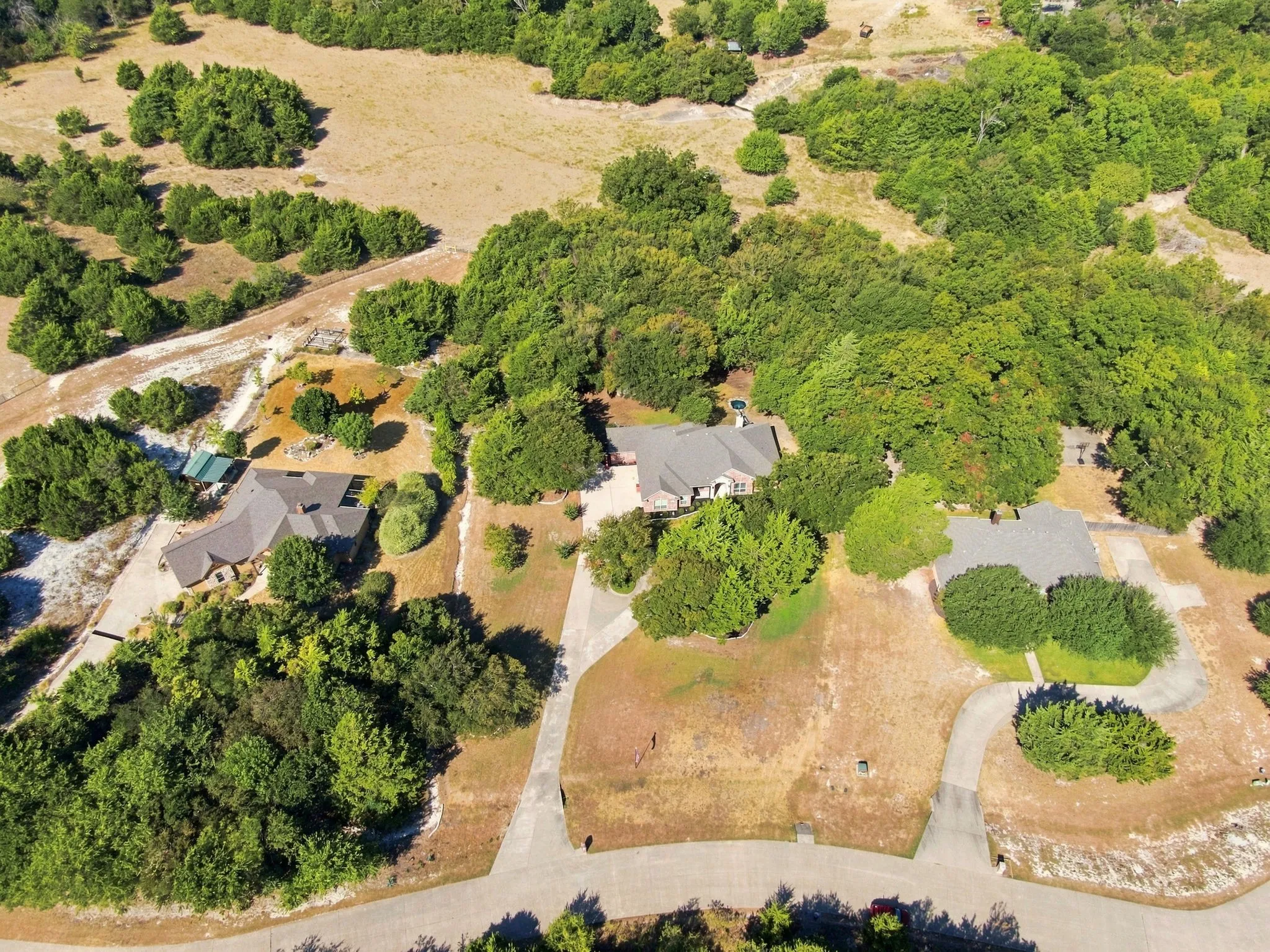 Aerial view showcasing the full property, including three distinct residences, mature trees, and paved driveways.