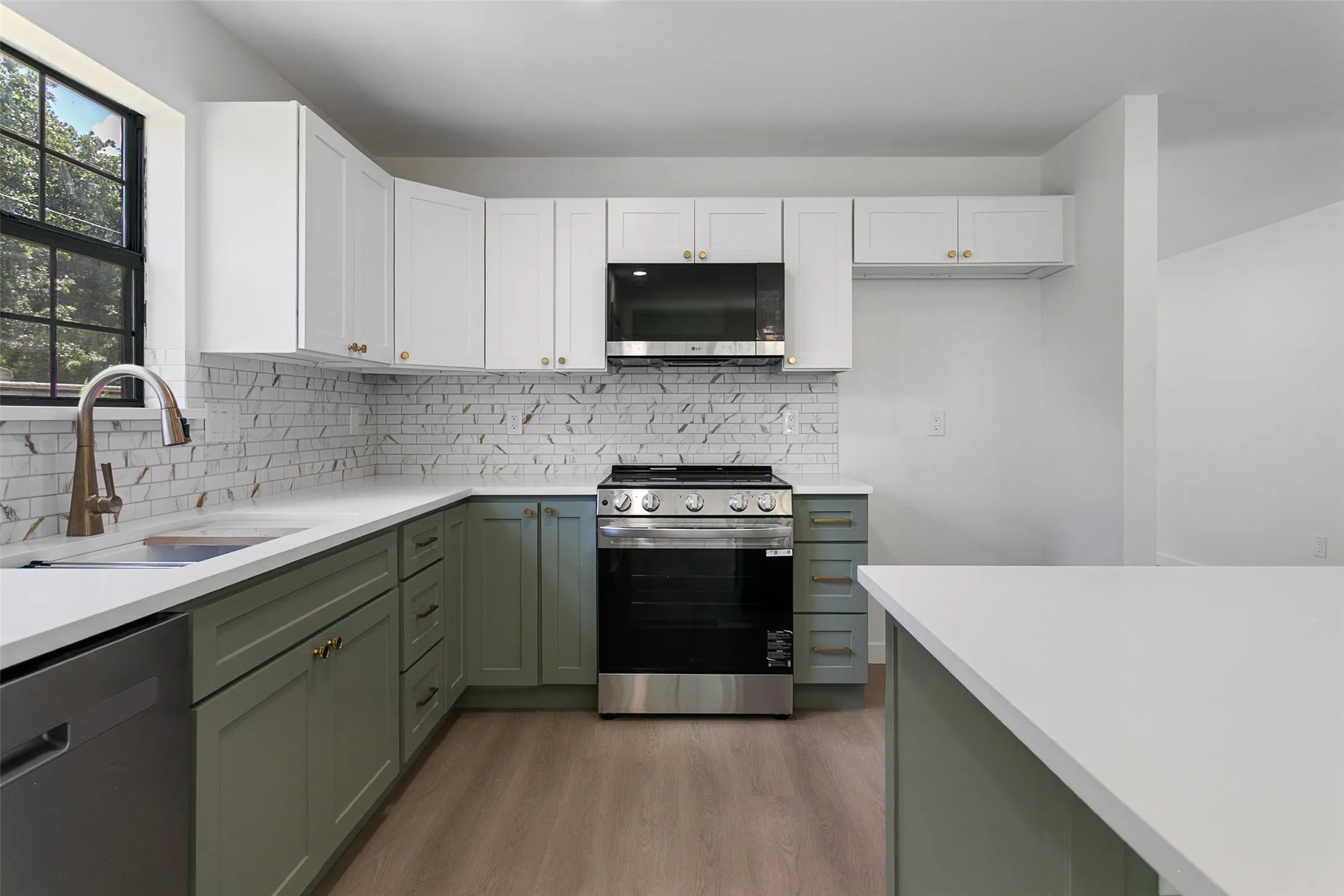 Two-tone cabinetry with gold-finish hardware, stainless steel range, light-toned countertops, and wood-finish flooring