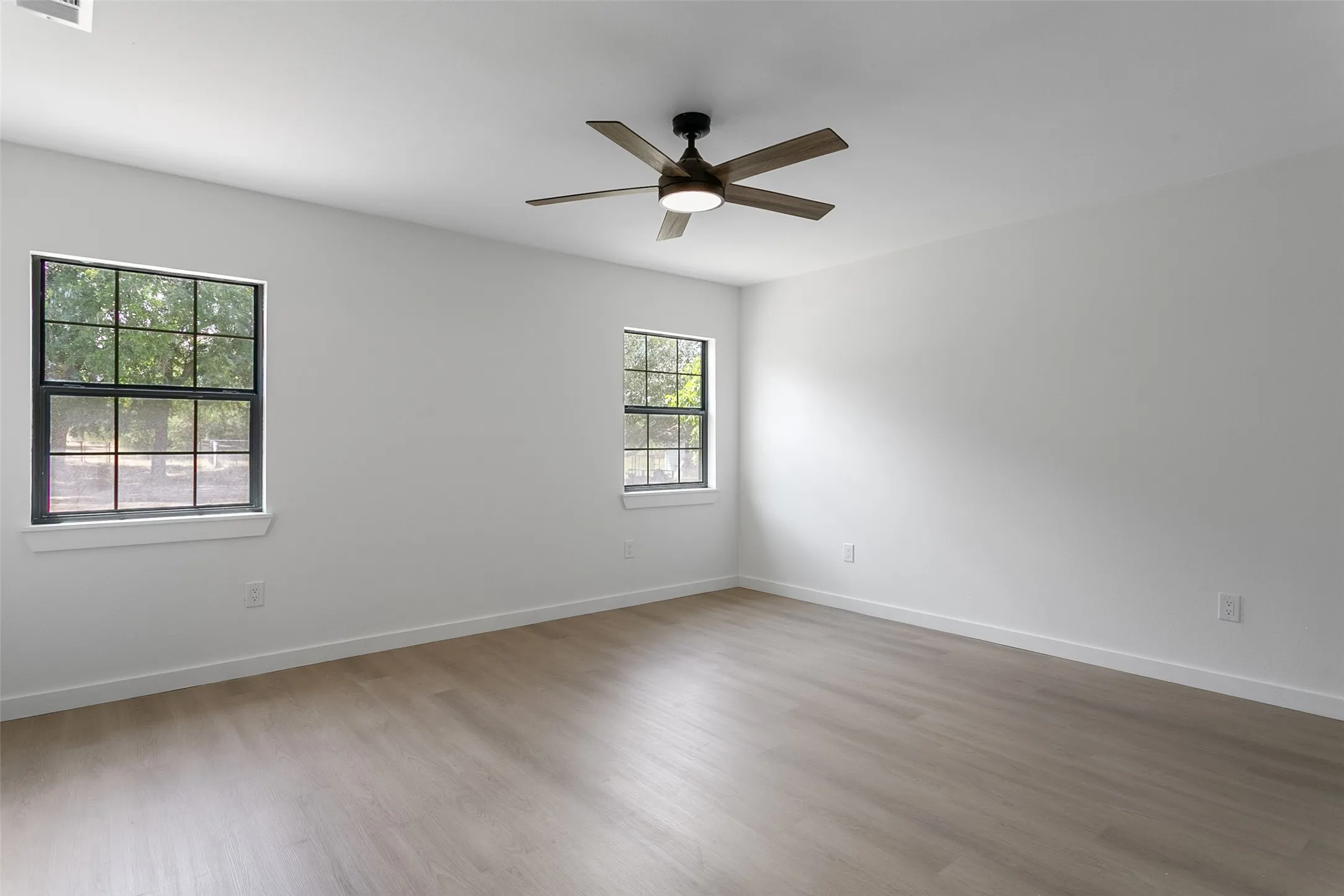 Spacious interior featuring wood-finish flooring, white walls, and two windows with dark frames
