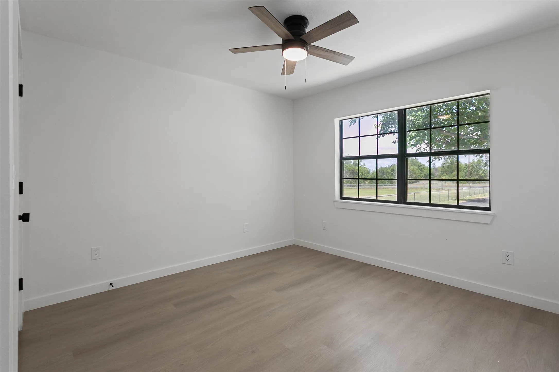 Neutral wall paint, wood-finish flooring, ceiling fan with integrated lighting, and a multi-pane window with black trim