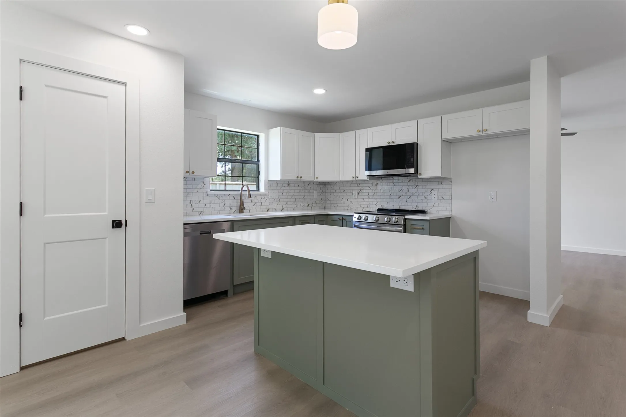 Modern kitchen featuring a central island with a solid surface countertop, two-tone cabinetry, stainless steel appliances, and wood-finish flooring