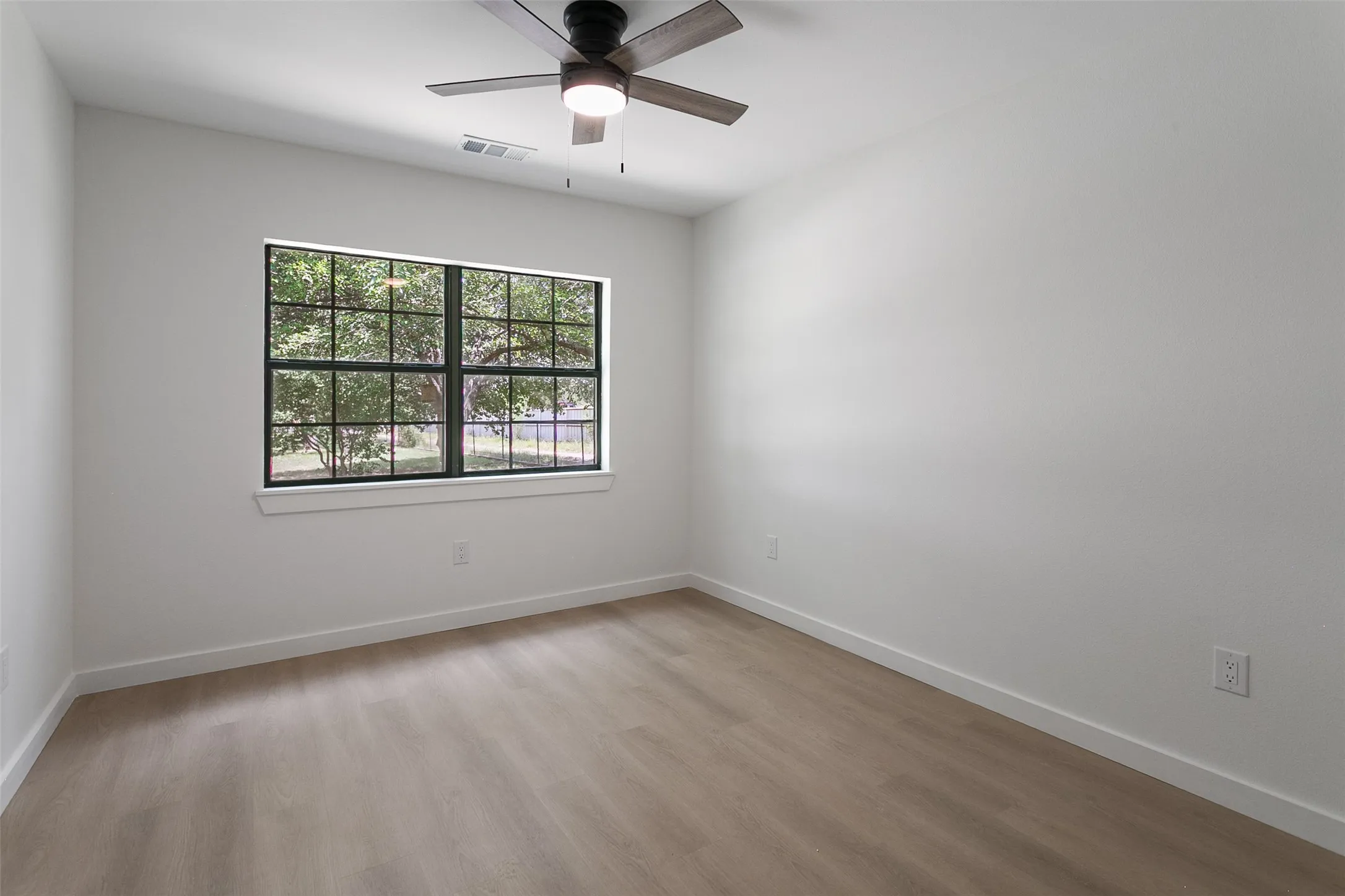 Room with a large window featuring black gridded panes, a modern ceiling fan, and light wood-finish flooring