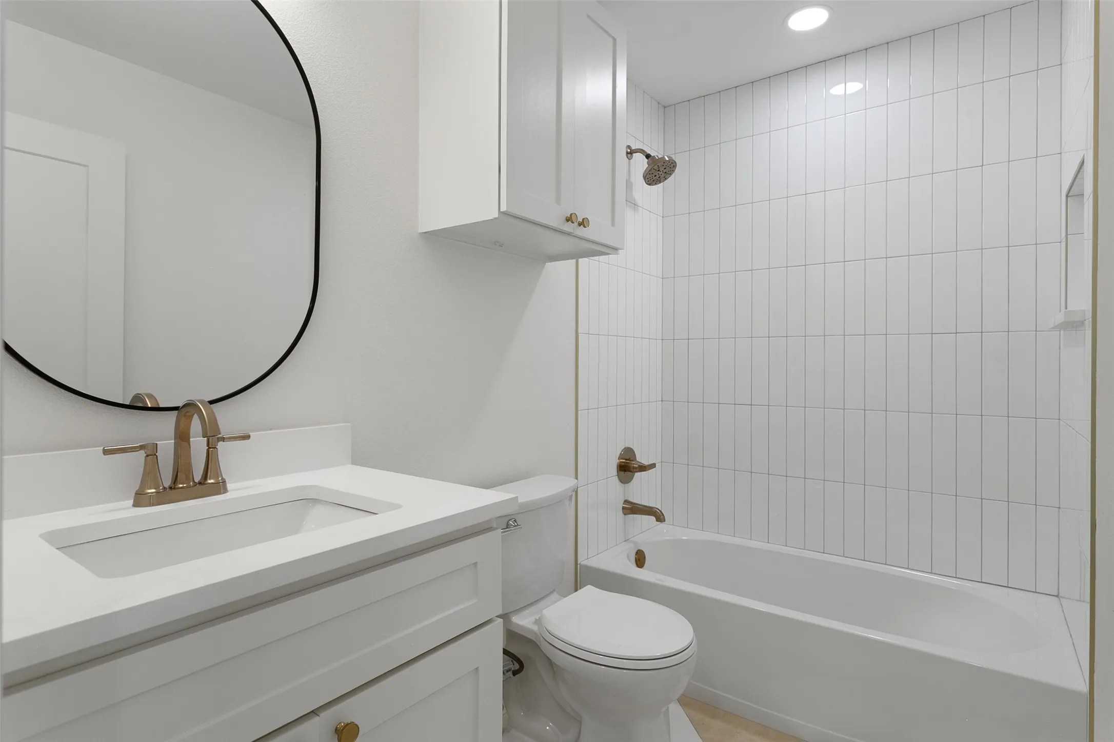 Bathroom featuring a vanity with an integrated sink, a bronze-finish faucet, a black-framed mirror, a toilet, and a bathtub with vertical tile surround