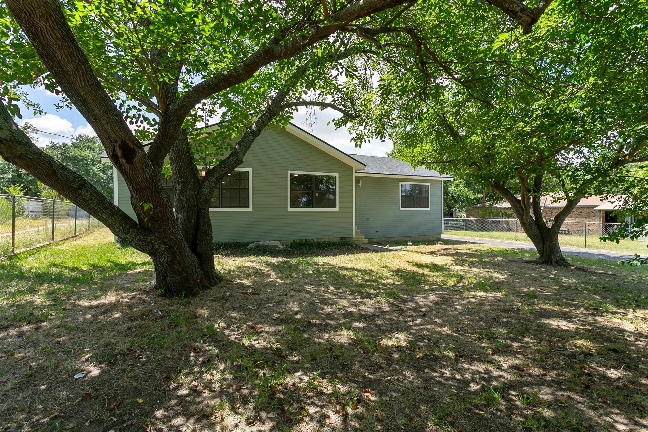 Green exterior siding with white window trim, dark window frames, and a dark roof