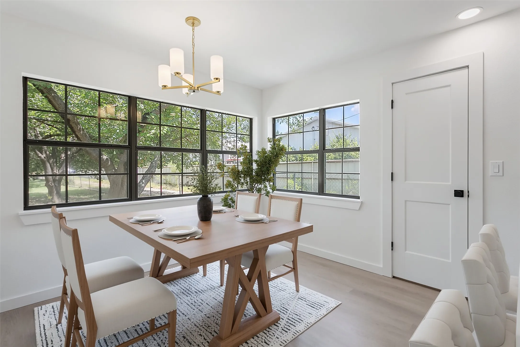 Light wood-finish flooring, white walls, and a modern gold-finish chandelier
