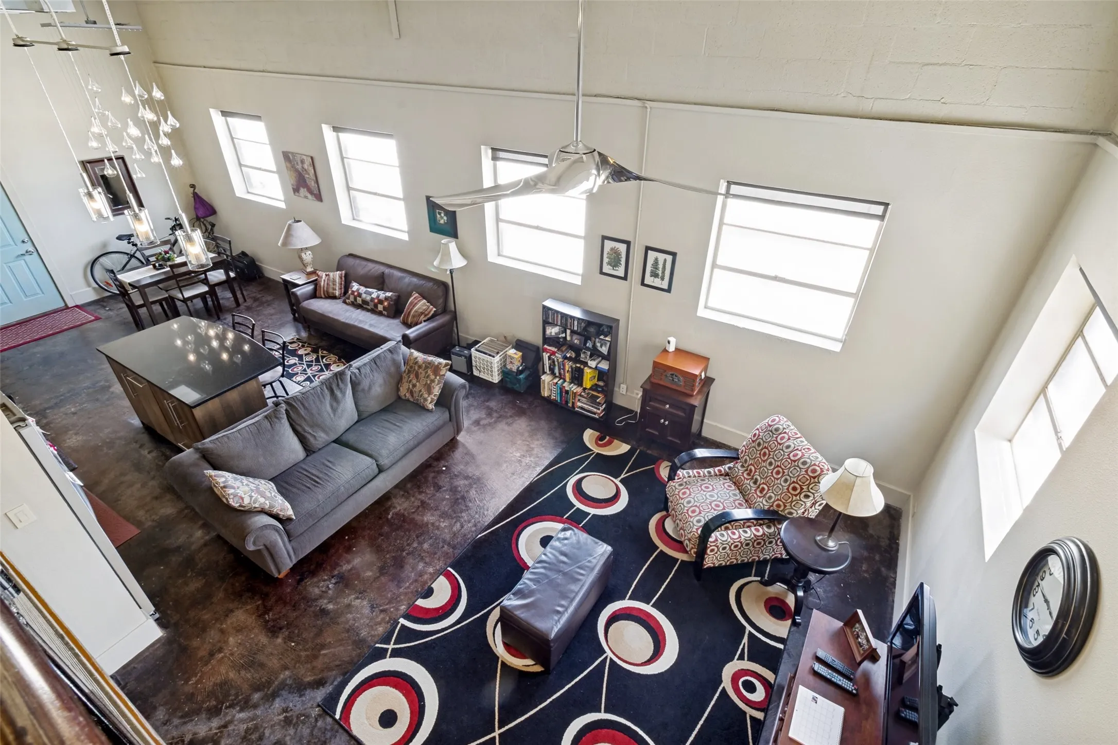 Soaring ceilings with multiple high-set windows, polished concrete flooring, a modern ceiling fan