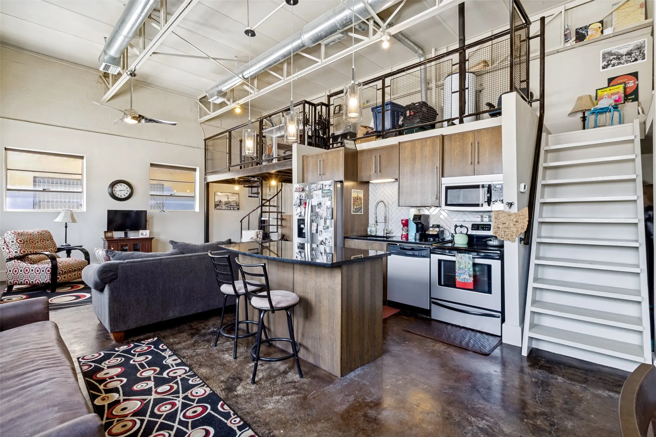 Exposed ductwork, concrete flooring, kitchen island, ladder like stairs near the entrance and a spiral staircase on the other end to get upstairs