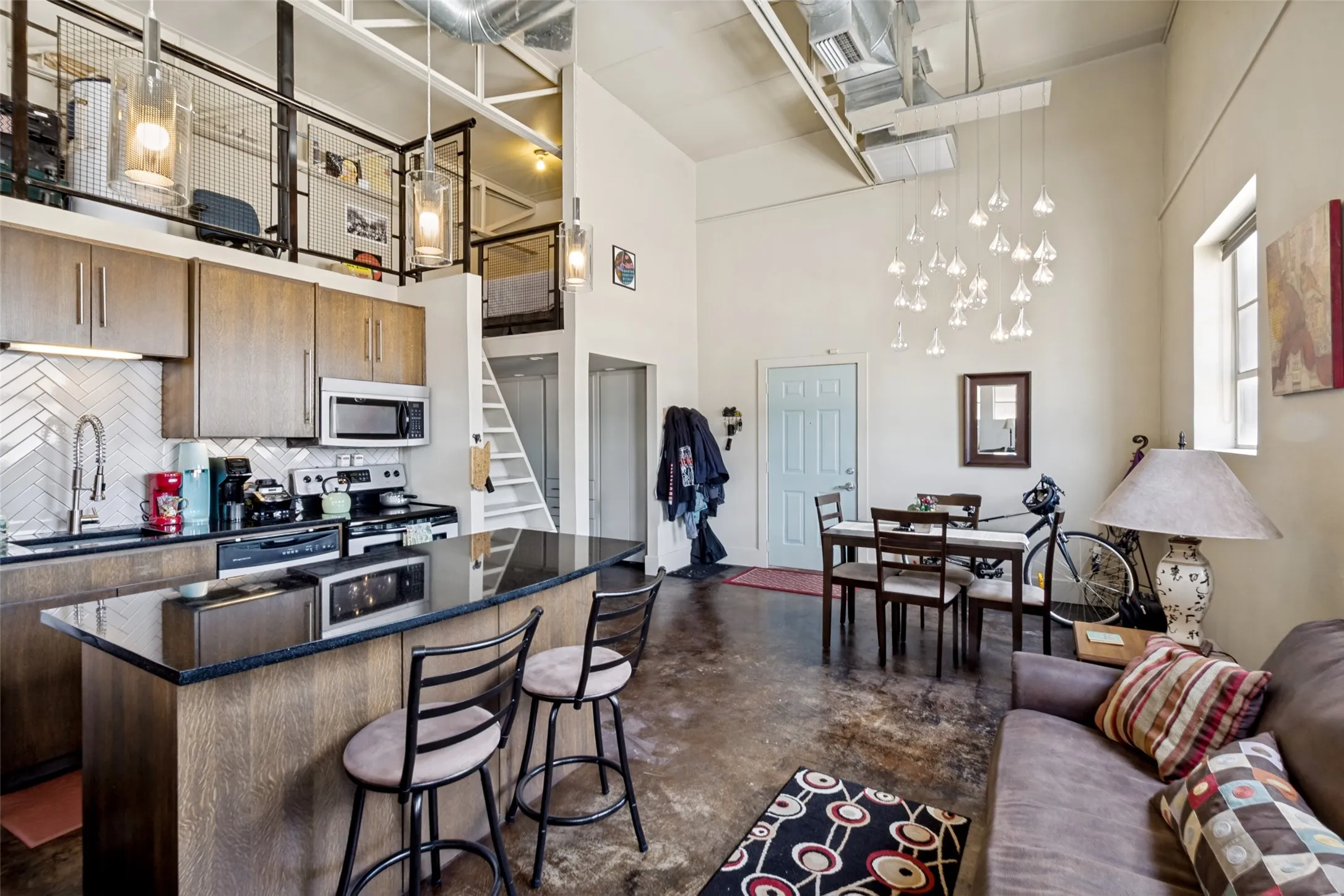 Open-concept living space with concrete flooring, a mezzanine level, high ceilings, and exposed ductwork