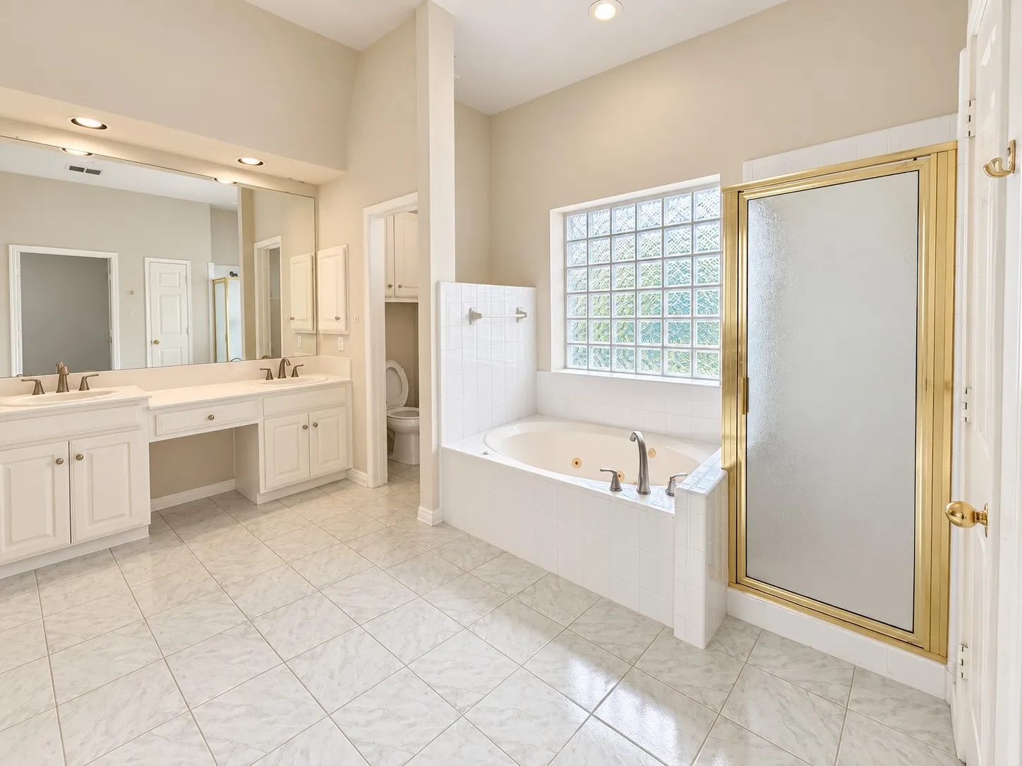 Dual vanities with integrated sinks, built-in cabinetry, tiled flooring, an alcove bathtub with a glass block window, and a shower enclosure with a gold-tone frame