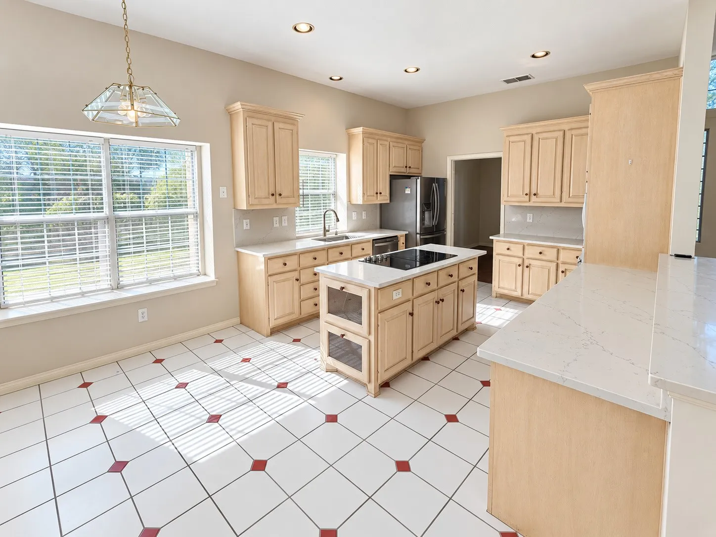 Kitchen featuring light wood cabinetry, white countertops, tile flooring with red accents, and a central island with a built-in cooktop
