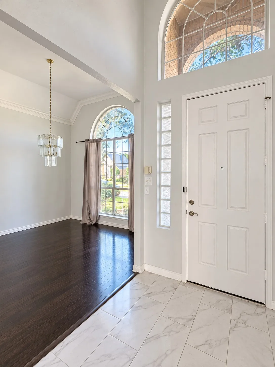 Two-story entry featuring an arched transom window and a contemporary chandelier