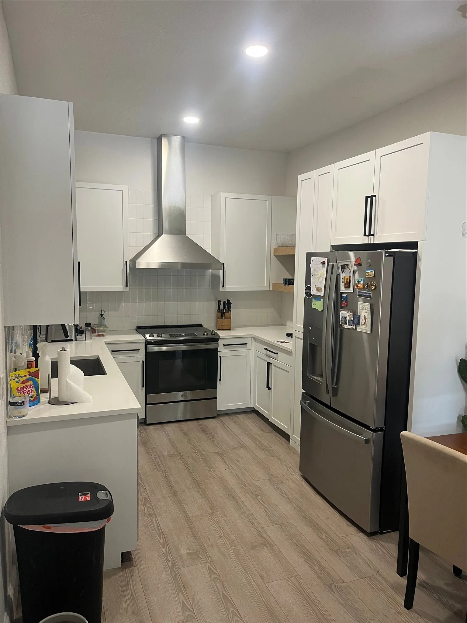 Modern kitchen featuring white shaker cabinetry, stainless steel appliances, light-toned wood-finish flooring, recessed lighting, and white countertops