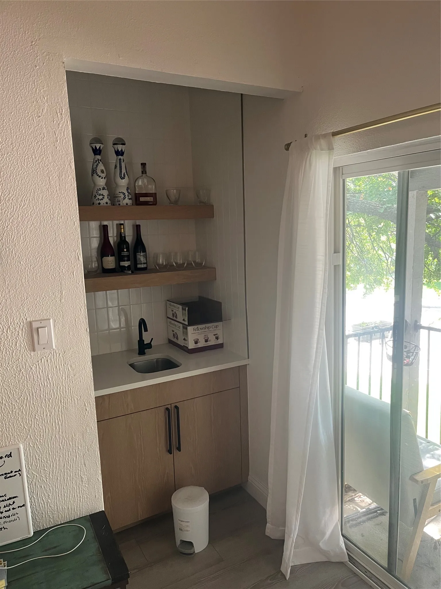 Compact wet bar featuring wood-finish cabinetry, a single basin sink with a matte black faucet, and two integrated wood-finish floating shelves