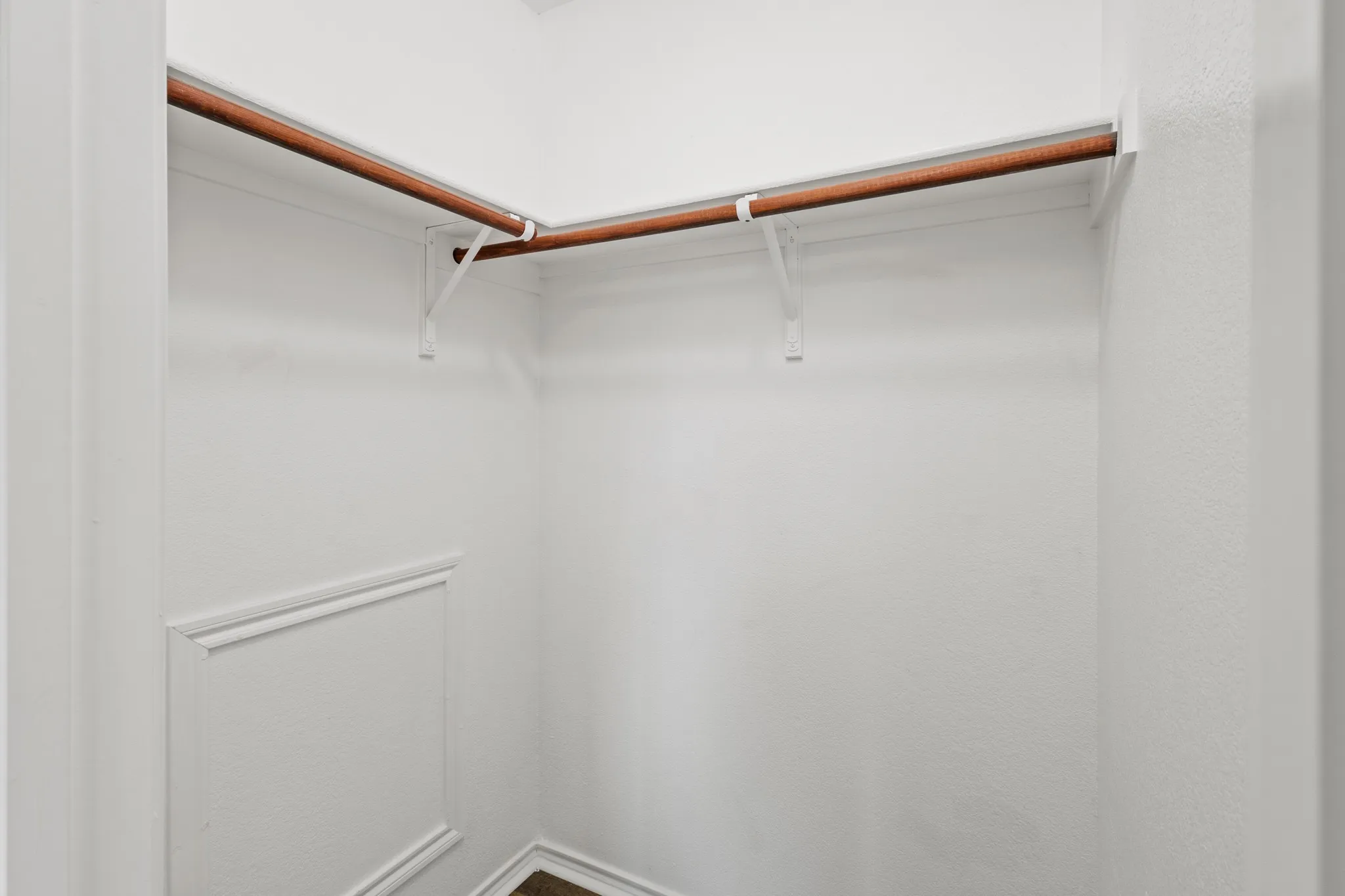 White-painted closet with wood-finish hanging rods and panel molding