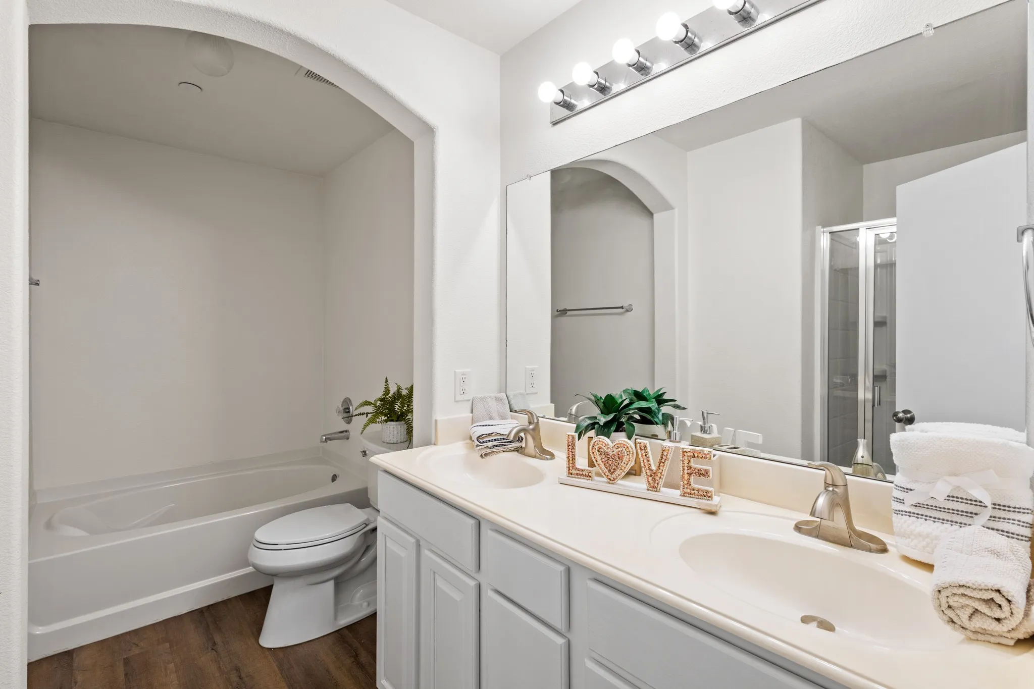 Double vanity with undermount sinks, wood-finish flooring, and a bath/shower combination in the primary bedroomn