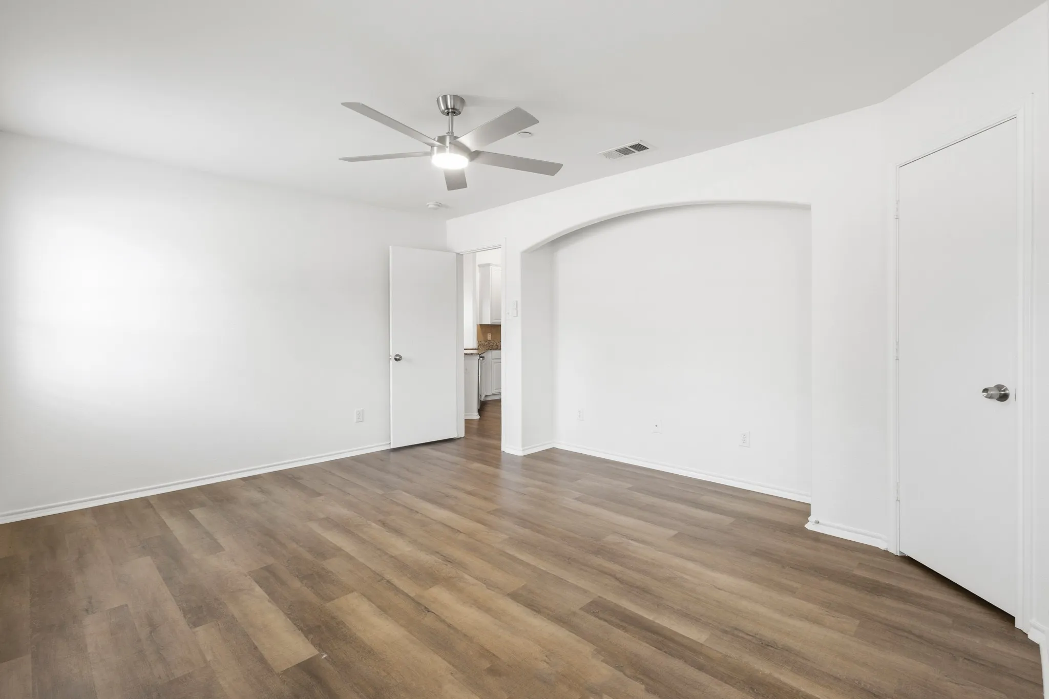 Wood-finish flooring, ceiling fan with integrated lighting, arched wall niche, and white interior doors