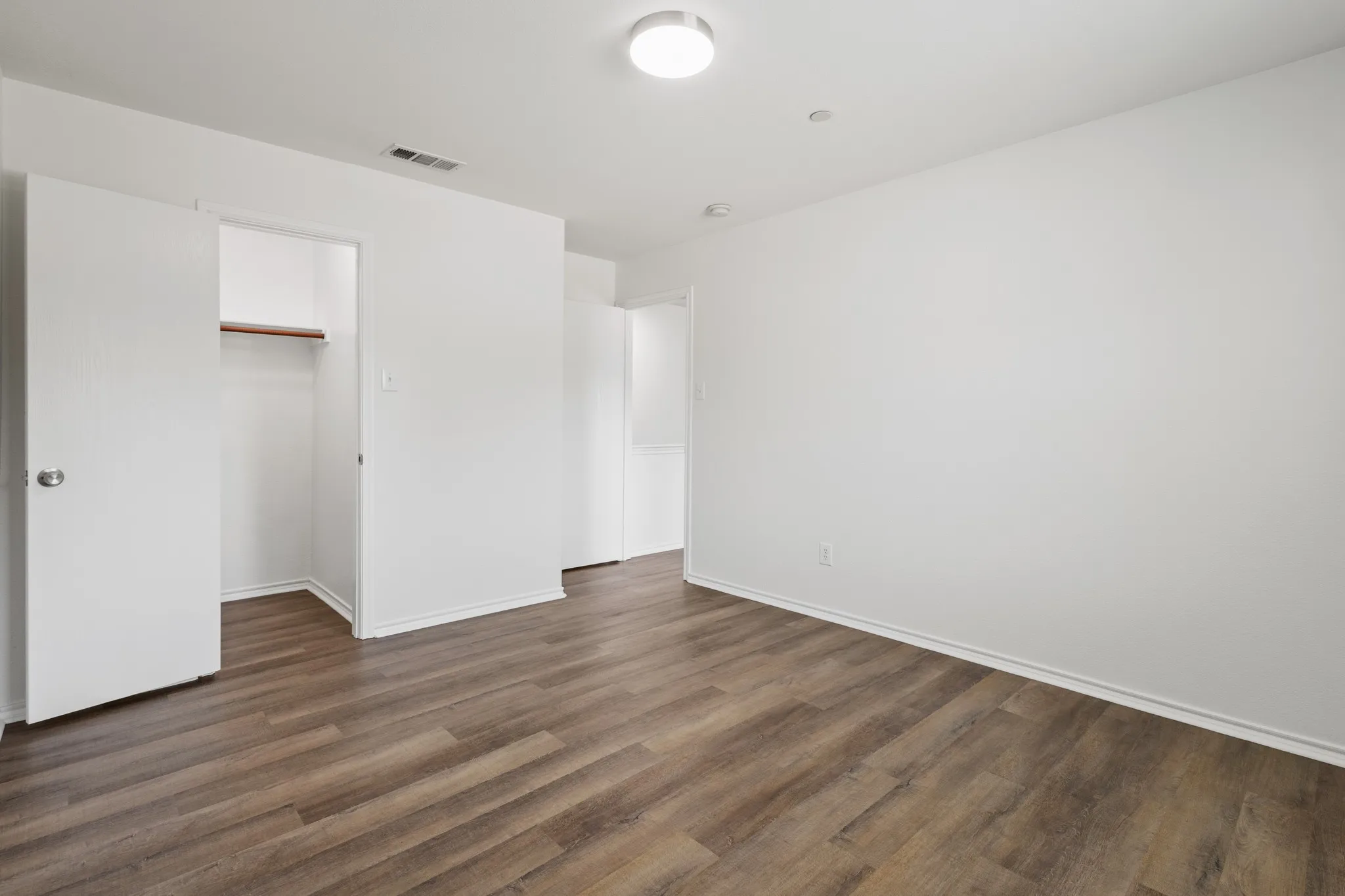 Neutral wall color, wood-finish flooring, white trim, recessed lighting, and a closet with built-in shelving
