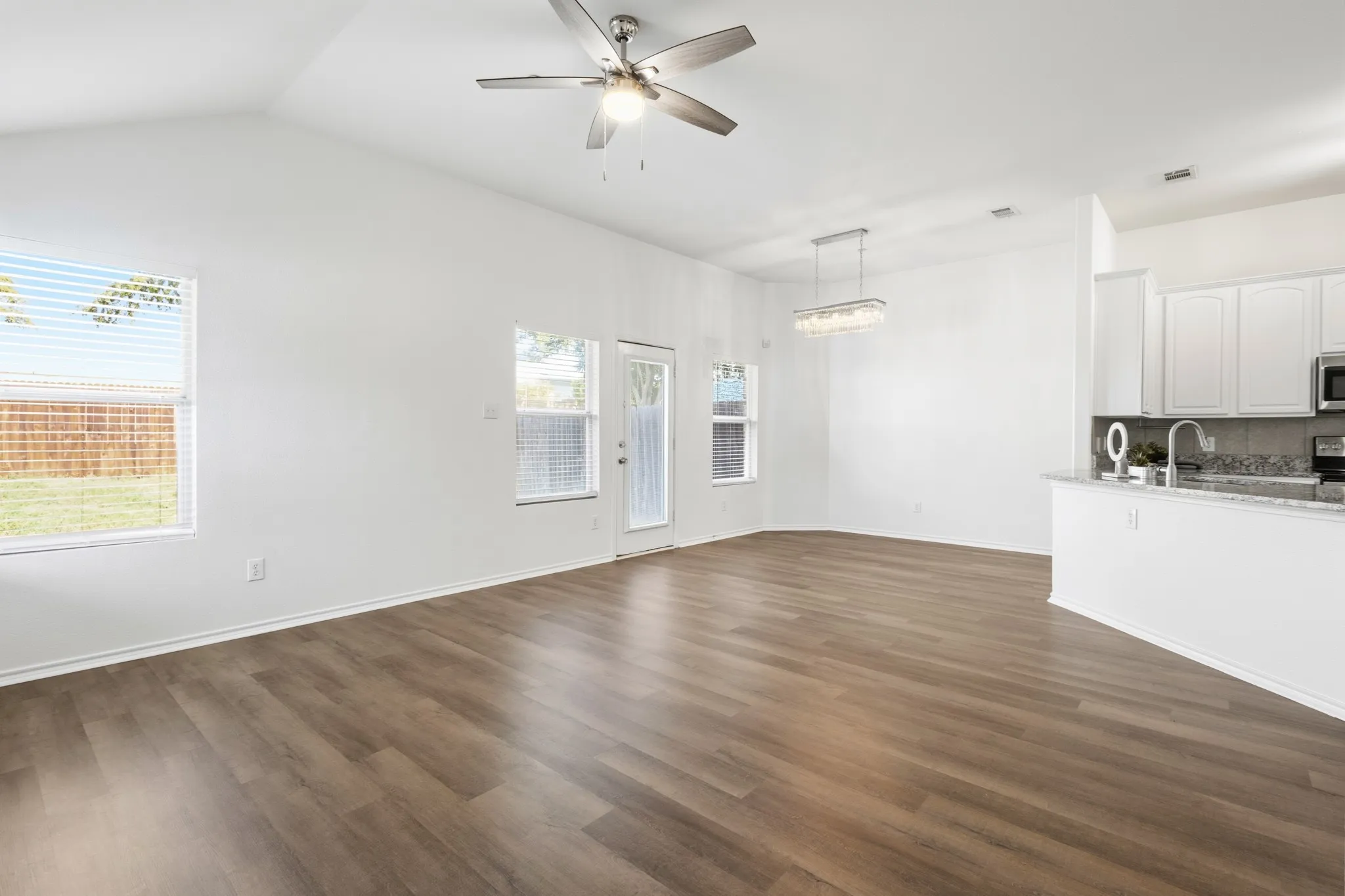 Vaulted ceiling with a contemporary ceiling fan, wood-finish flooring, white cabinetry, granite countertops, and stainless steel appliances