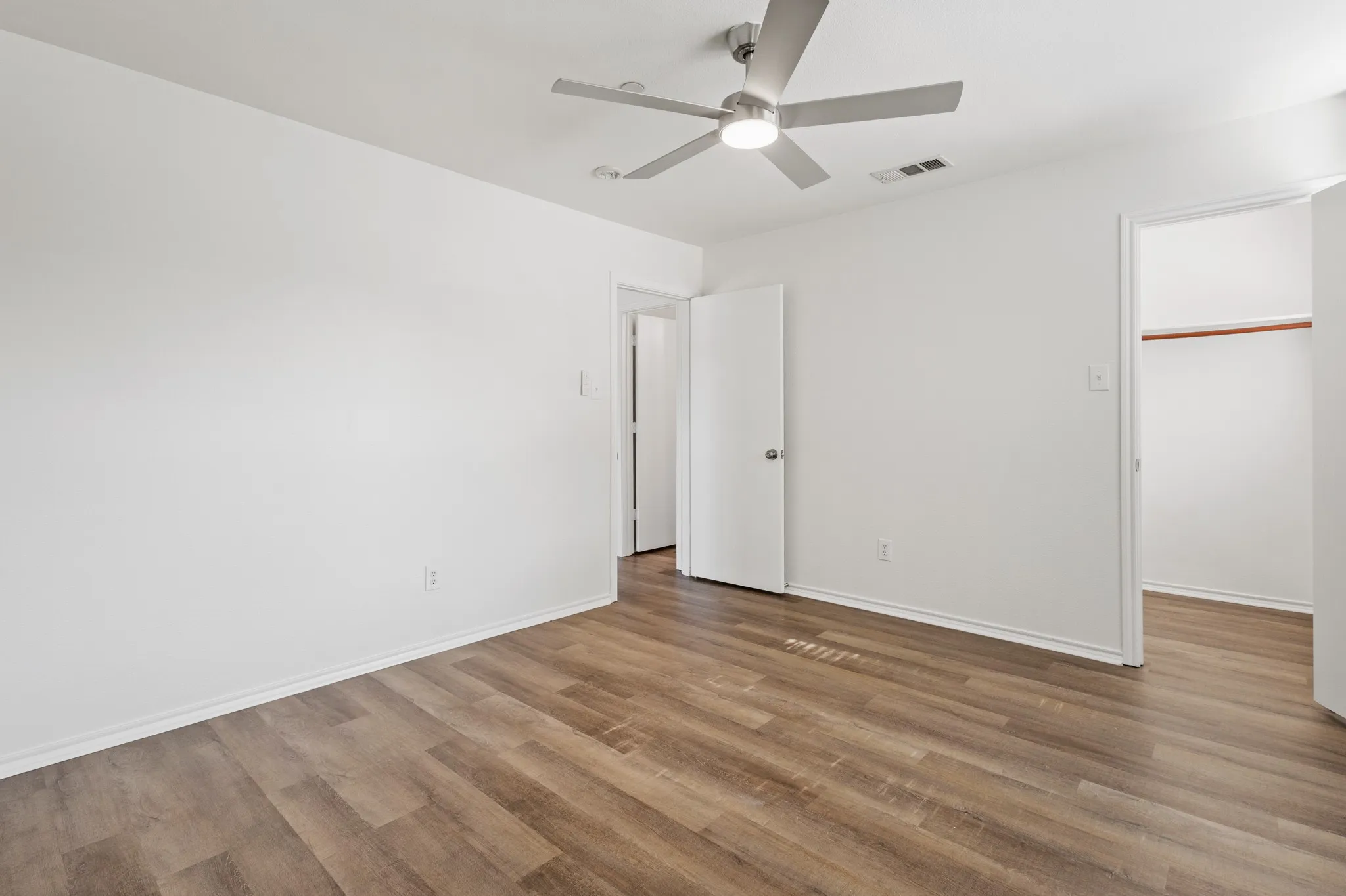 Wood-finish flooring, white painted walls, and a ceiling fan with integrated lighting