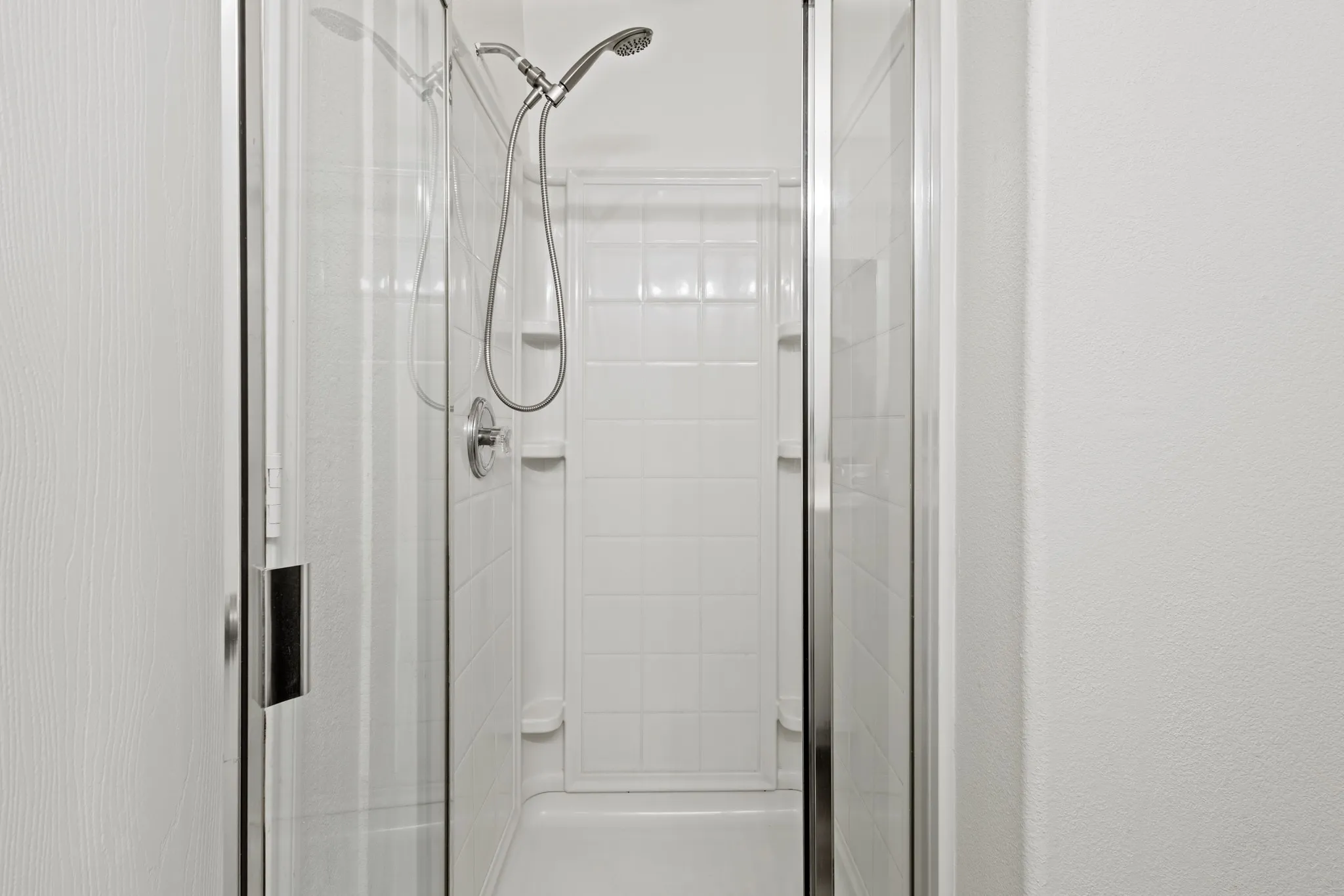 Shower enclosure with clear glass doors, white tiled walls, and a chrome shower fixture