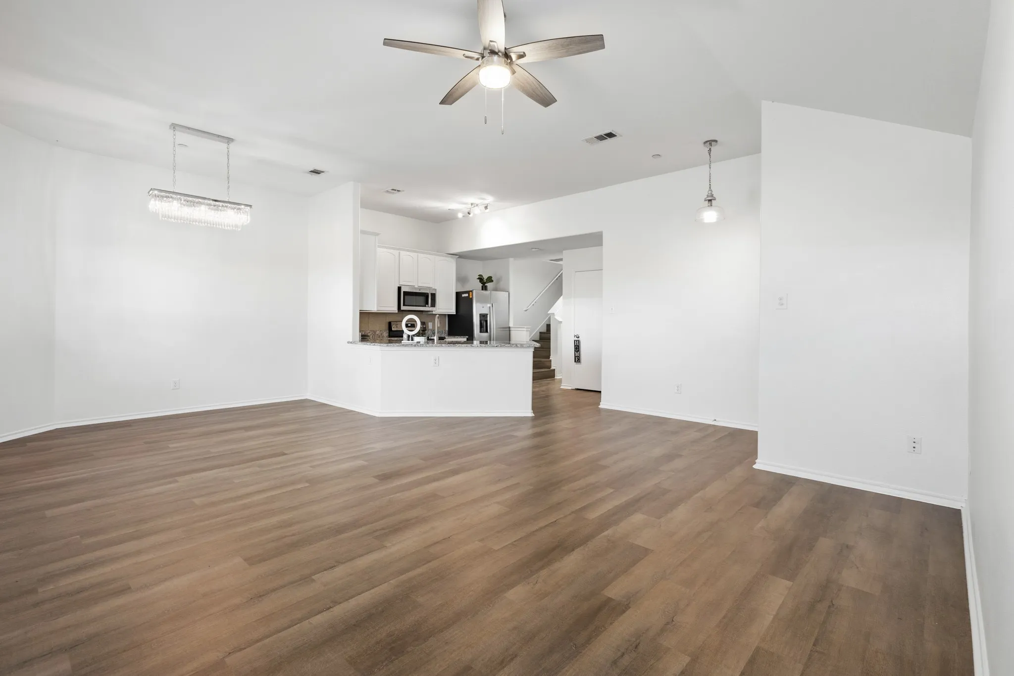 Open-concept living area featuring wood-finish flooring, a modern chandelier, and a ceiling fan