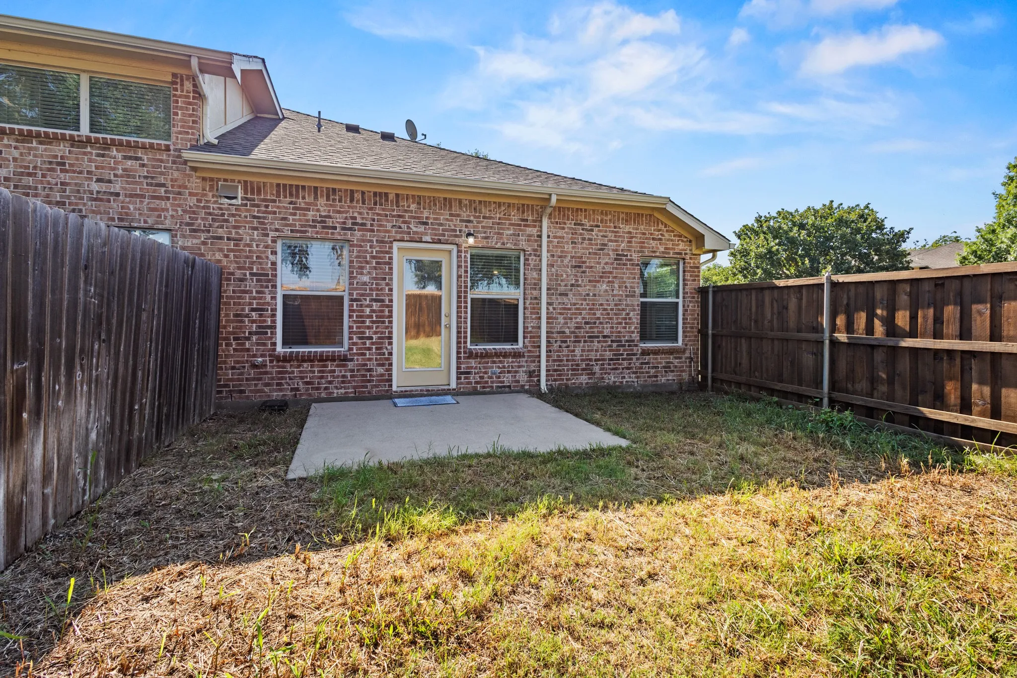 Brick exterior with multiple windows and a rear door, complemented by a concrete patio slab and wood privacy fencing