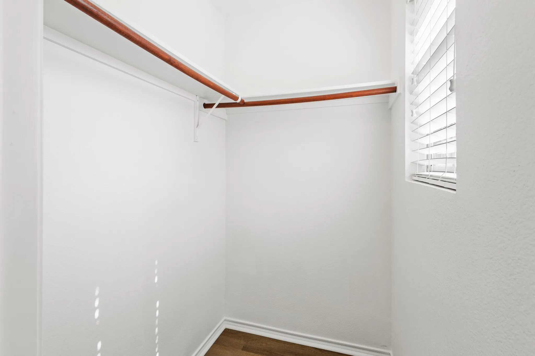 Walk-in closet with wood-finish flooring, white walls, built-in shelving, and a window with horizontal blinds