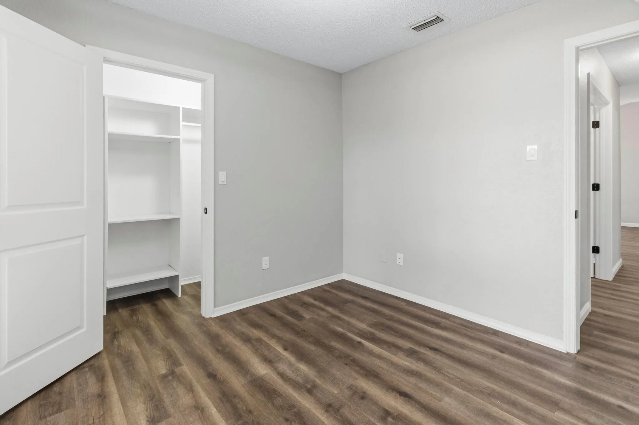 Room with wood-finish flooring, light grey walls, and a white interior door