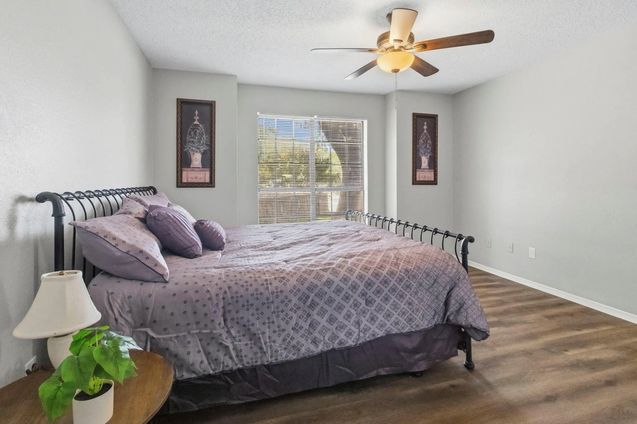 Wood-finish flooring, ceiling fan, and window with exterior landscaping