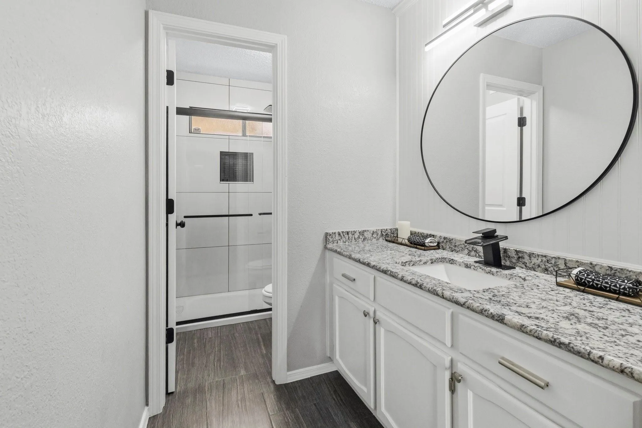 Bathroom featuring a white vanity with granite countertops, an undermount sink, and a black-framed circular mirror