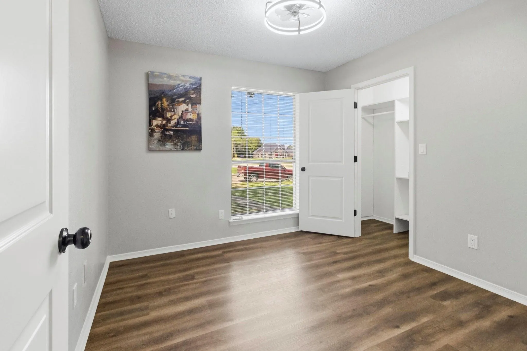Wood-finish flooring, white trim, a closet with built-in shelving, a ceiling-mounted light fixture, and a window with blinds