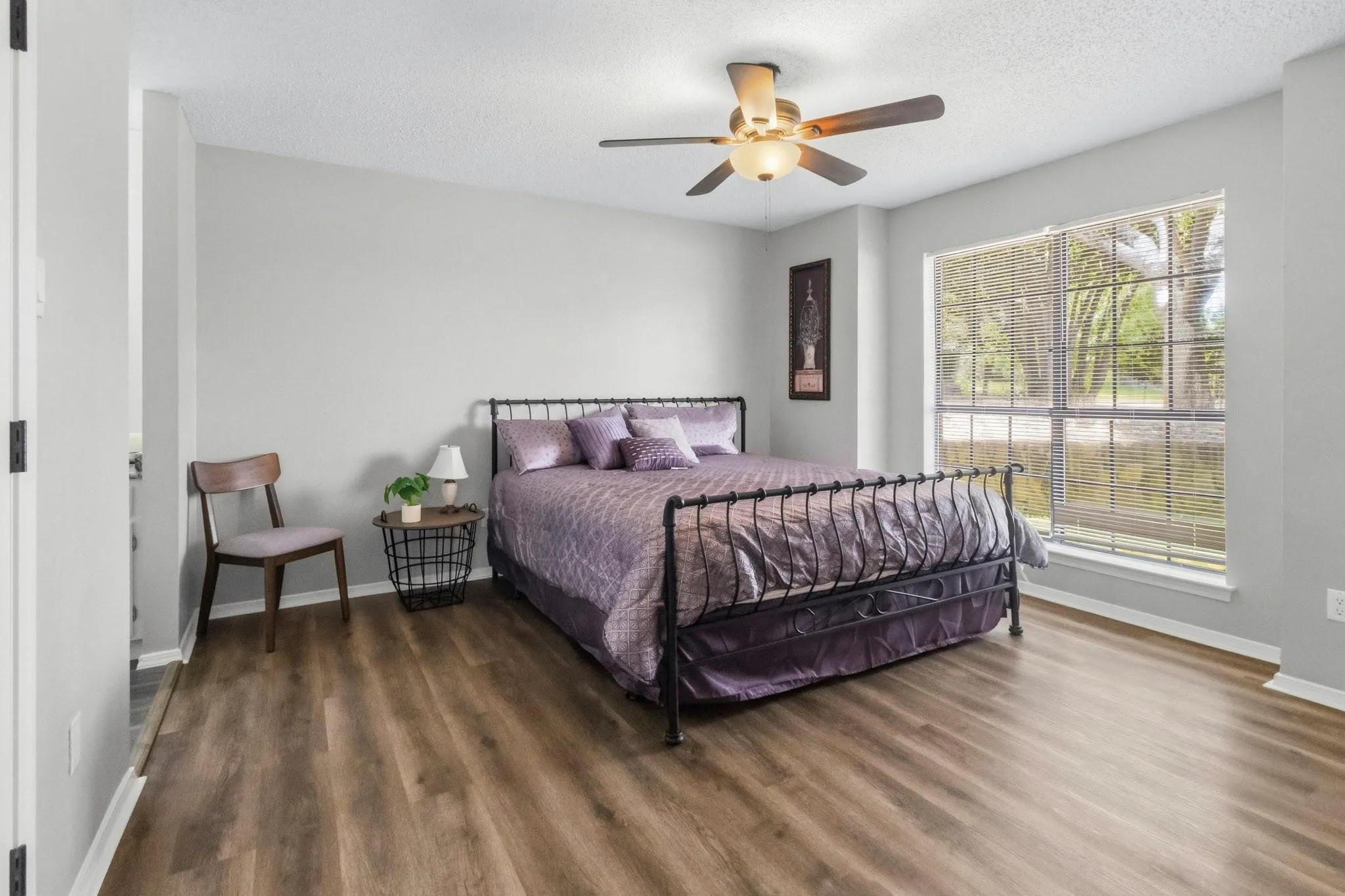Wood-finish flooring with light gray walls, a window with horizontal blinds, and a ceiling fan with integrated lighting