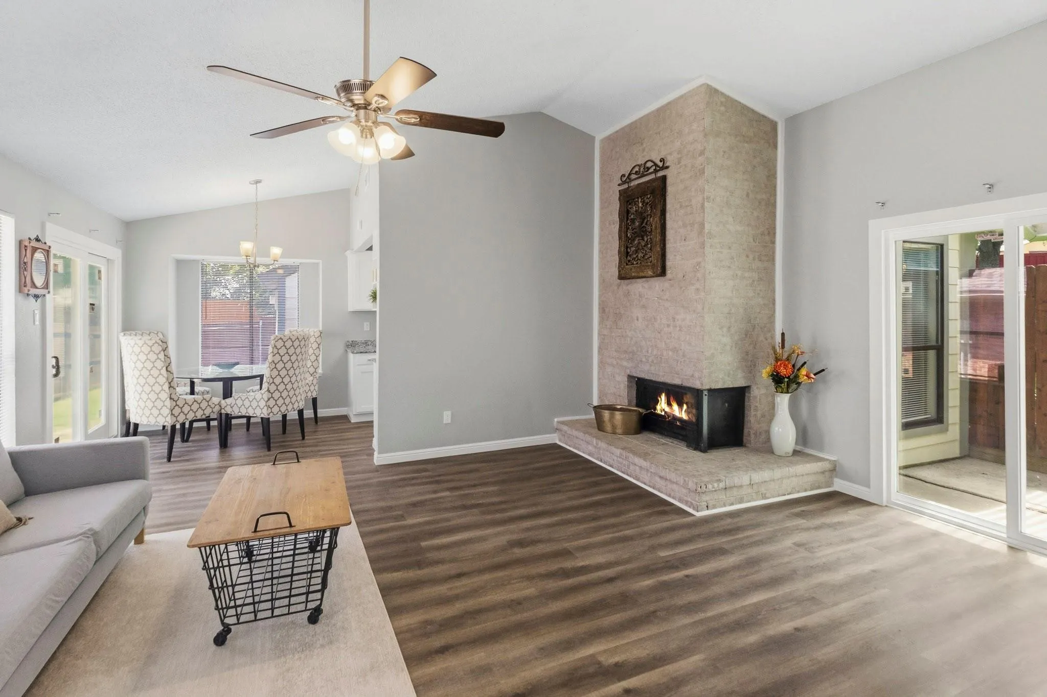 Vaulted ceiling, wood-finish flooring, stone-clad fireplace, ceiling fan with integrated lighting, and sliding glass door