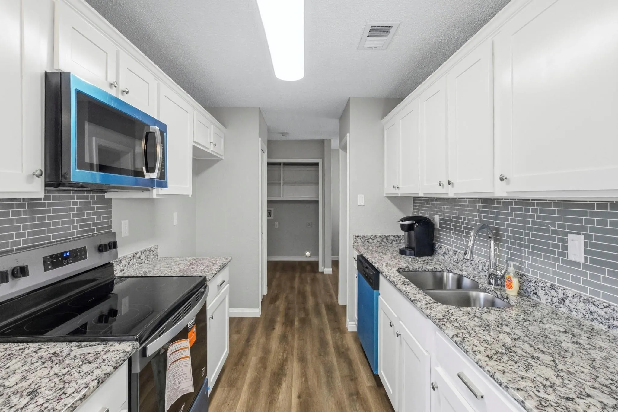 THE appliances still have the BLUE FILM on them to keep them NEW until the buyer moves in!! Kitchen featuring white cabinetry, light granite-style countertops, an undermount double basin stainless steel sink, a gray rectangular tile backsplash, and wood-finish flooring