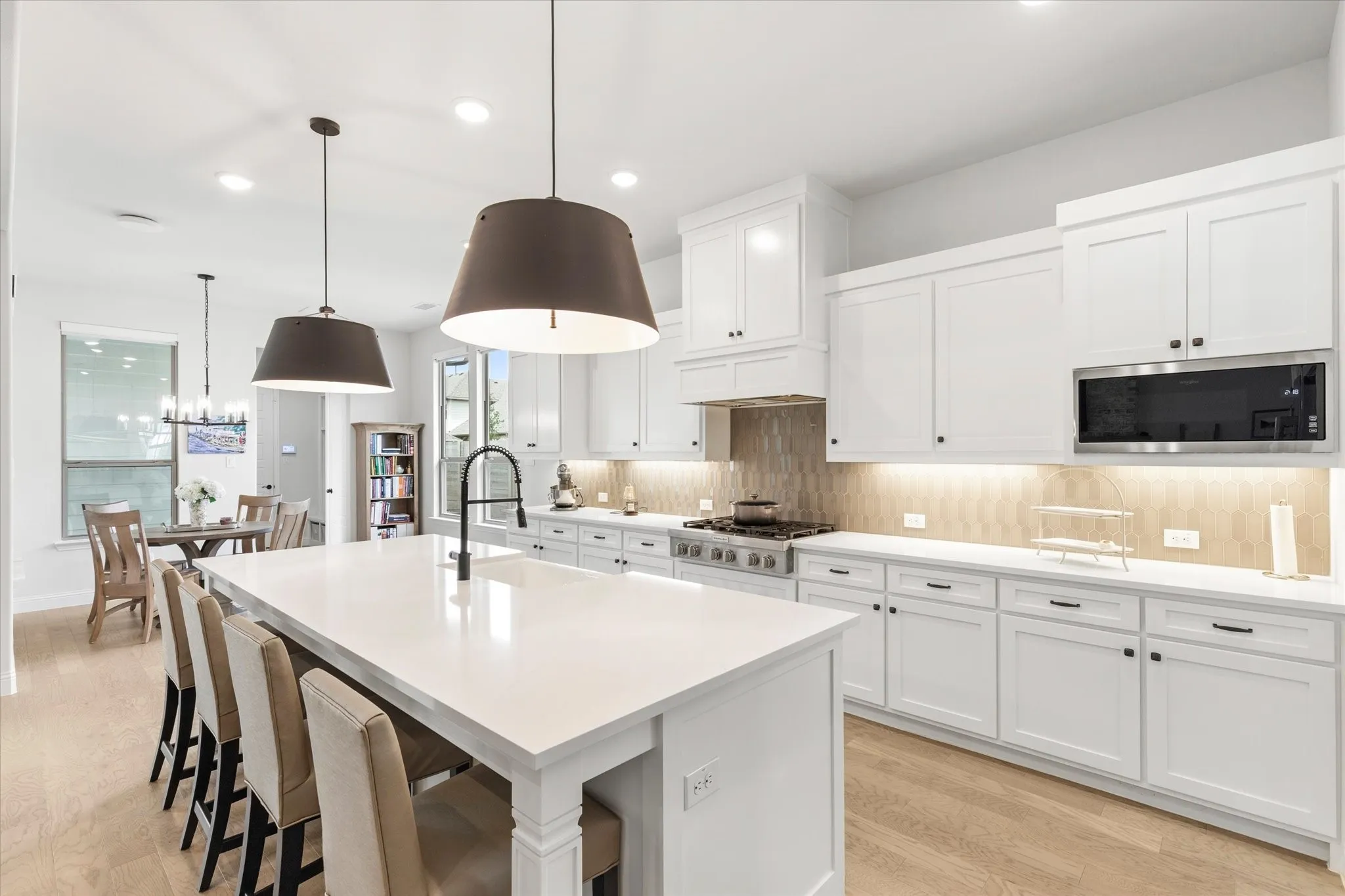 Open-concept kitchen and living area featuring a central island with a farmhouse sink, stainless steel appliances, and wood floorin.  Breakfast area to the right.
