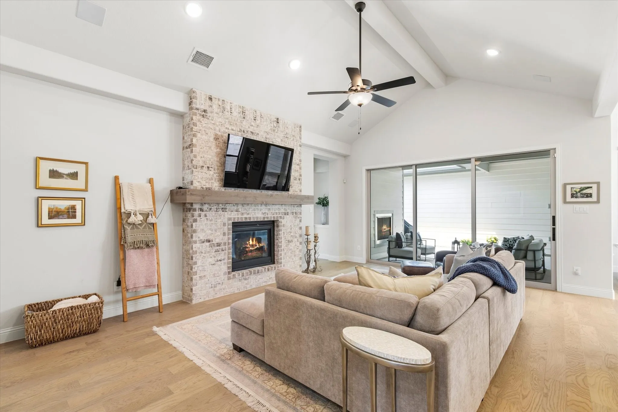 Vaulted ceiling with beams, recessed lighting, wood flooring, brick-surround fireplace with a wood mantle. Primary Bedroom is to the right, and the rear patio is through the glass sliding doors.