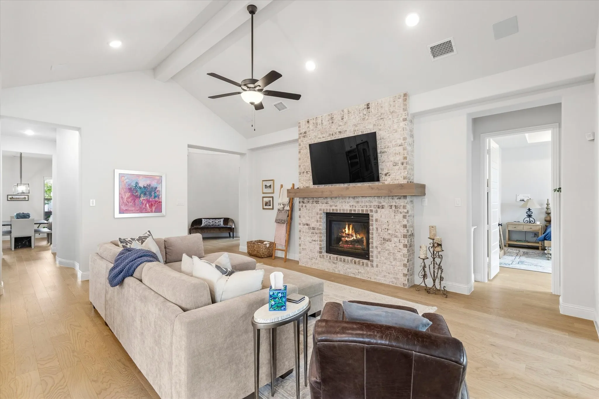 Cozy Living Area that opens into the Kitchen.  Brick Fireplace, wood flooring and Vaulted ceilings.  Hallway to the left leads to the Dining room, and the door to the right leads to the Primary Bedroom.
