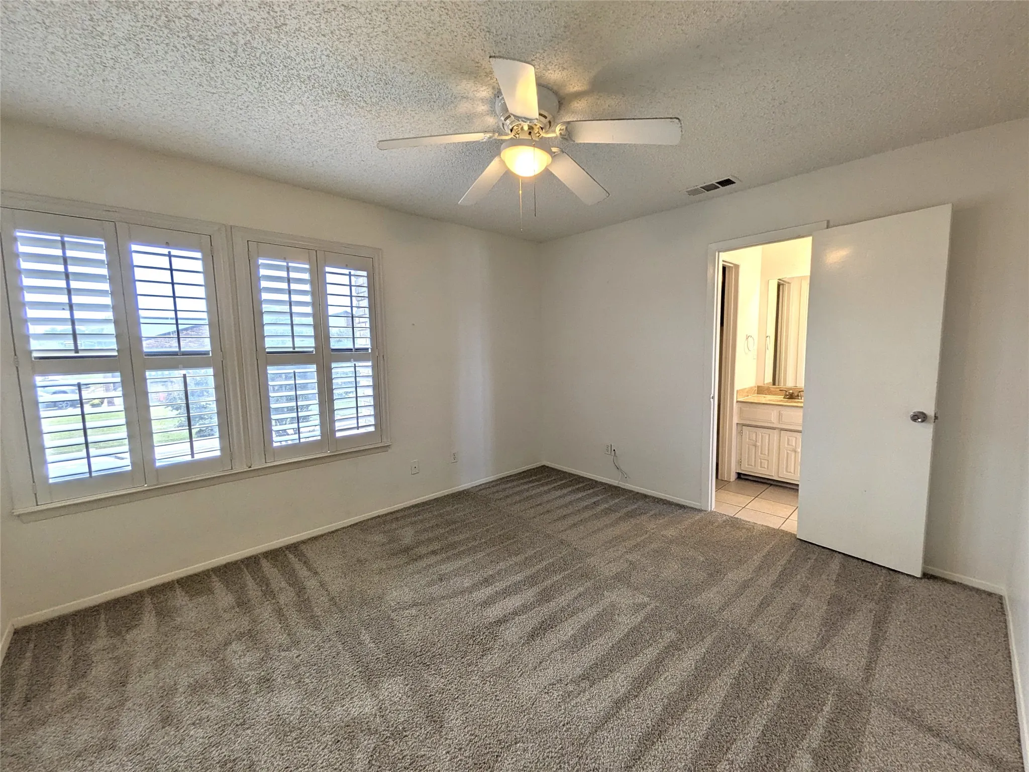 Bedroom featuring patterned carpeting, two windows with plantation shutters, and an overhead ceiling fan with lighting