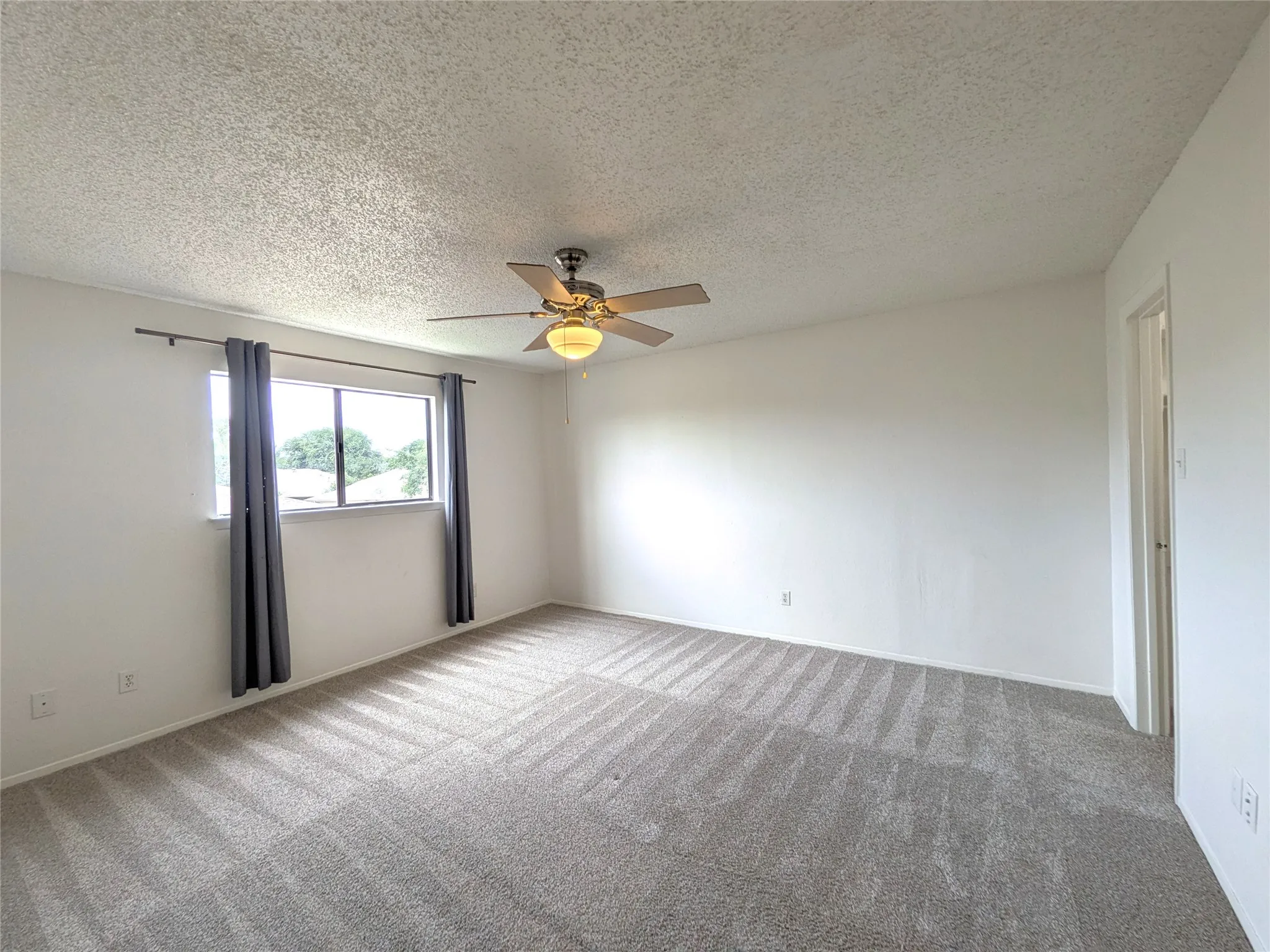 Carpeted room featuring a ceiling fan with integrated lighting, a window with a curtain rod, and light-colored walls