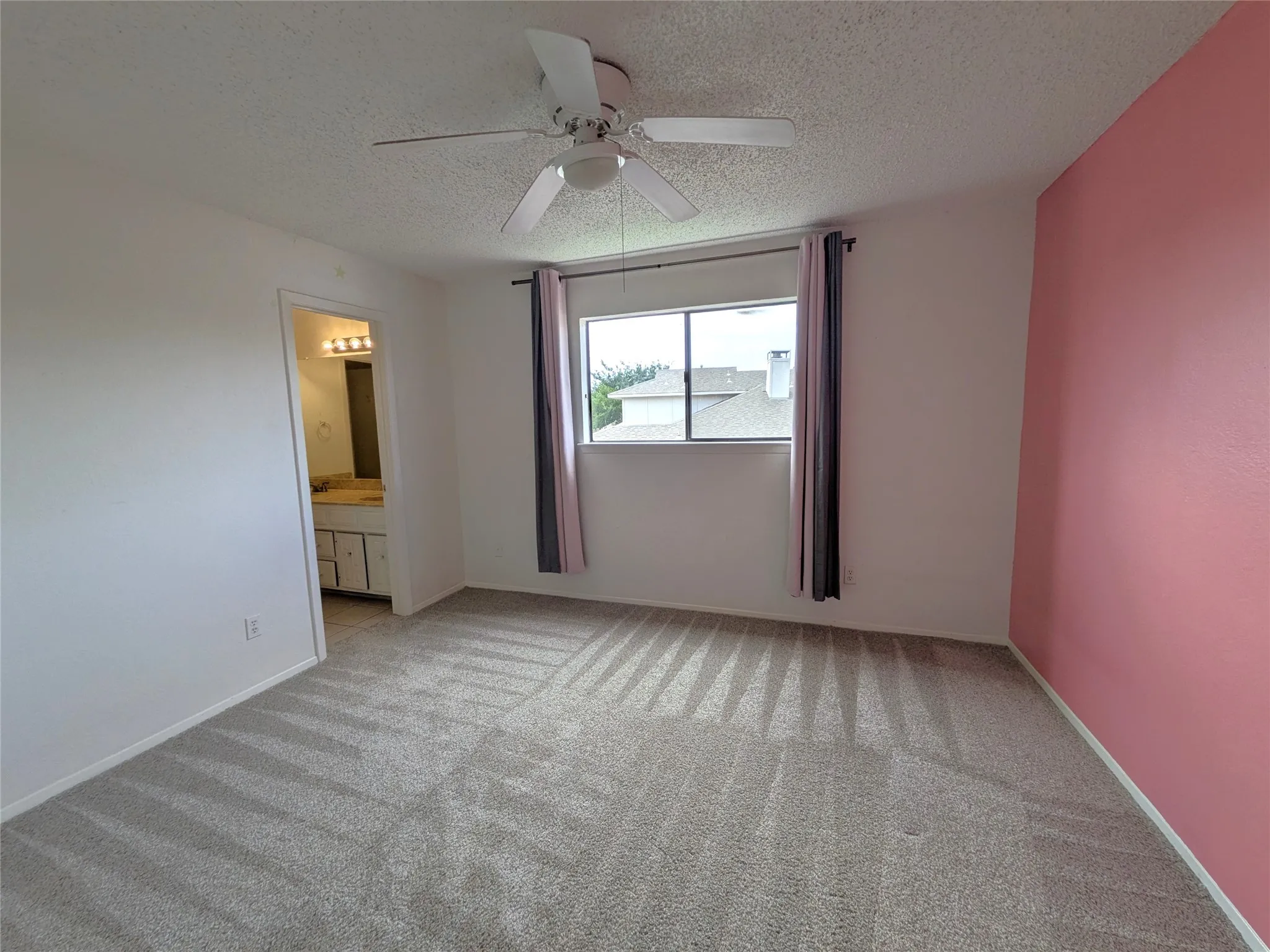 Carpeted interior space featuring a ceiling fan with integrated lighting, a window with exterior views, and a dedicated entry to a vanity area with a built-in cabinet