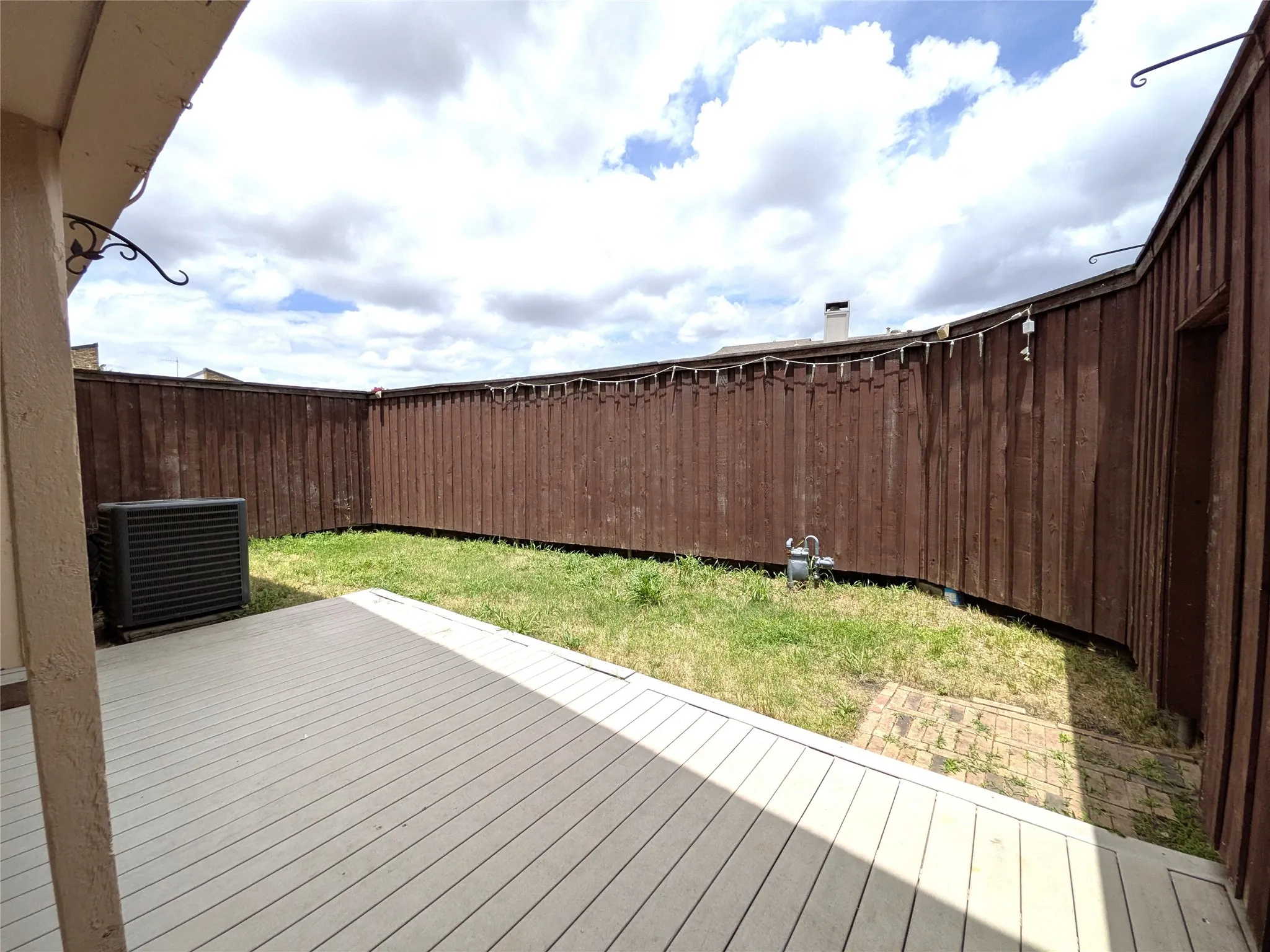 Outdoor deck area with a light-colored composite surface, surrounded by a tall brown wood privacy fence